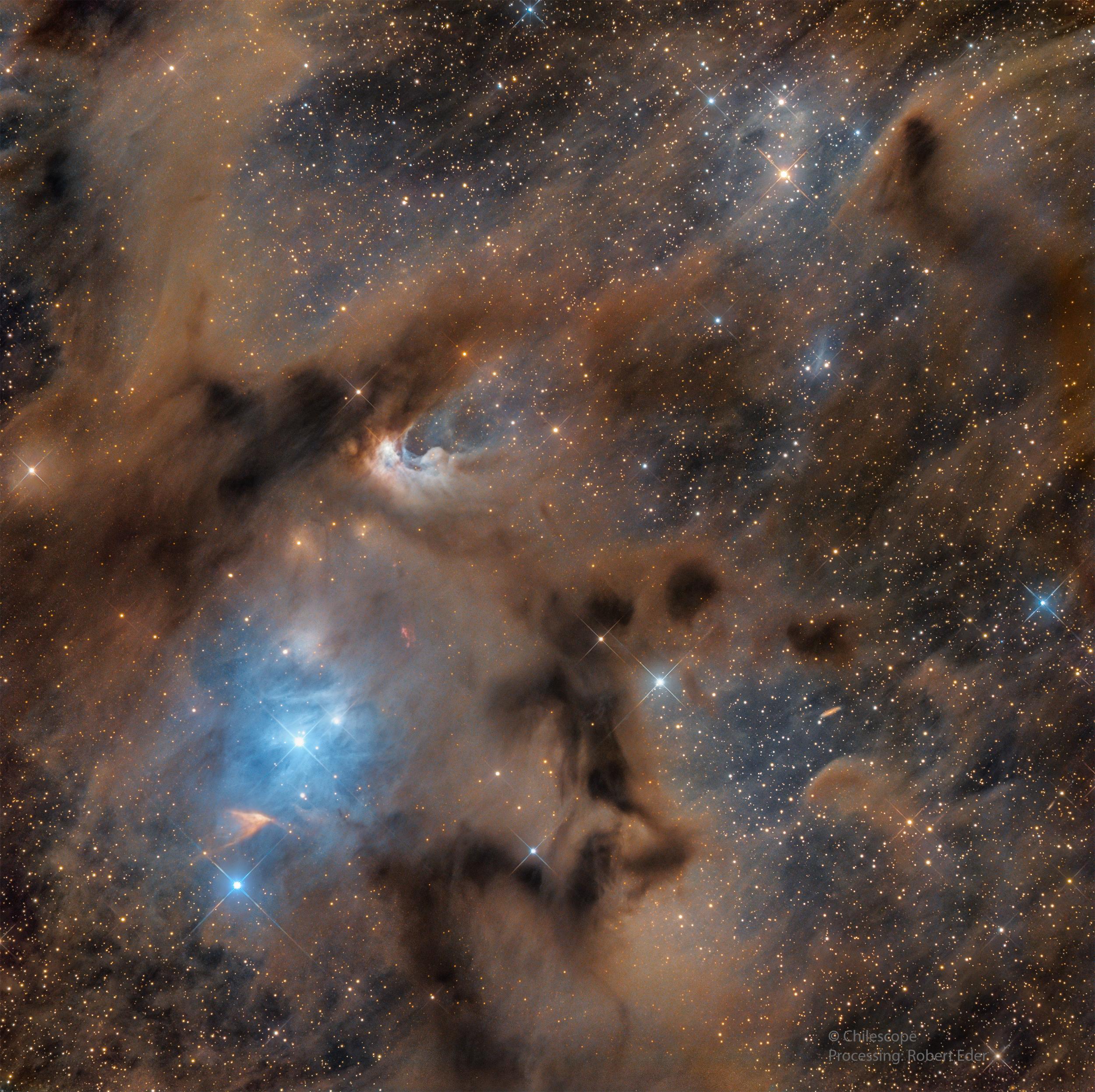 سُدم وأغبرة عاتمة بلون بني مع مناطق بلون أزرق مع وجود نجوم مدببة وتناثر نقاط النجوم المضيئة عبر الصورة