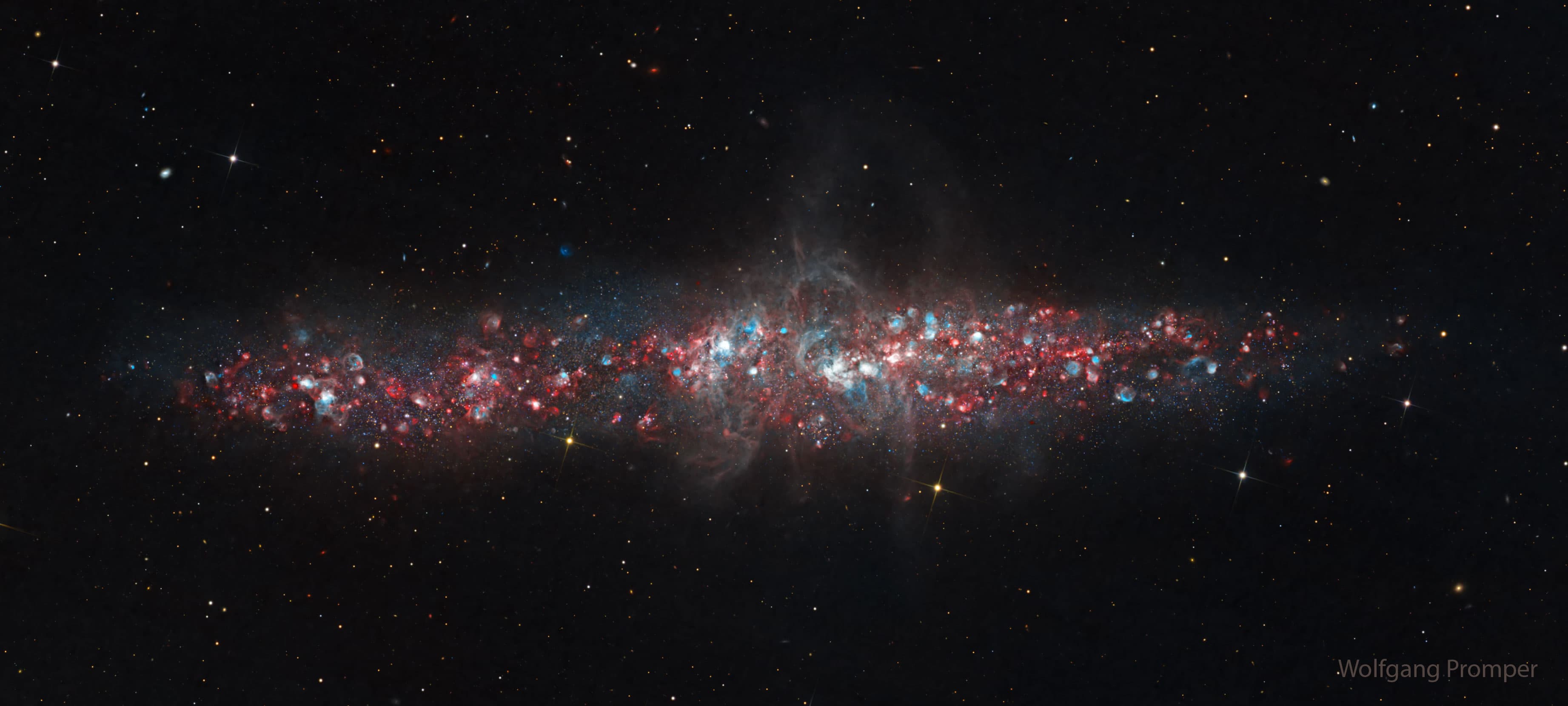 تظهر مجرّة فيها الكثير من النقاط الزرقاء والحمراء. المجرّة عبارة عن لطخة إهليلجيّة طويلة عبر المنتصف وليست حلزونيّة كلاسيكيّة.