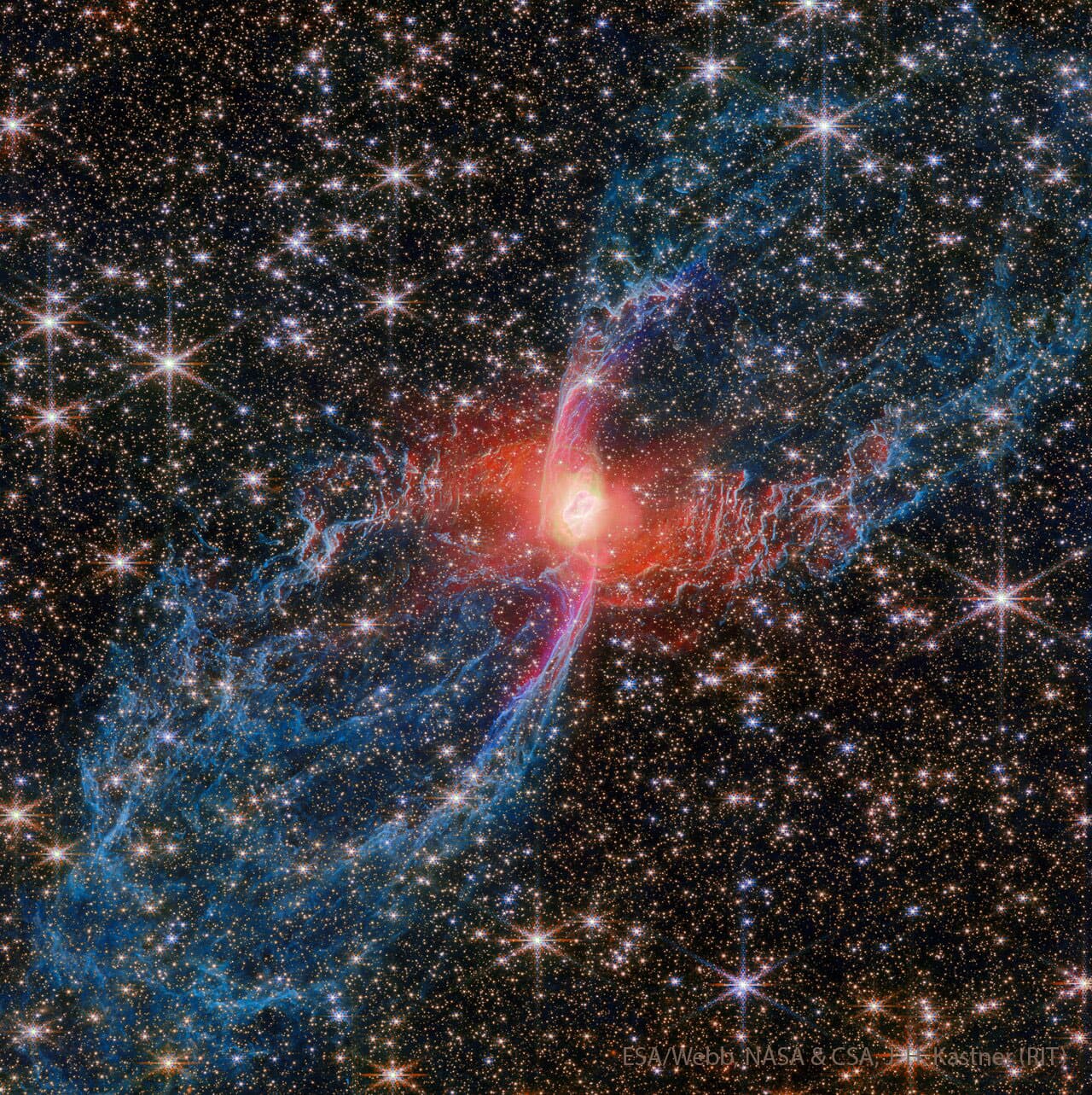 يُحيط حقلٌ نجميٌّ كثيفٌ بسديمٍ أزرق وأحمر يمتدّ من أسفل اليسار إلى أعلى اليمين. الأجزاء الخارجيّة للسديم زرقاء وخيطيّة، بينما الجزء الداخليّ أحمر وساطع.