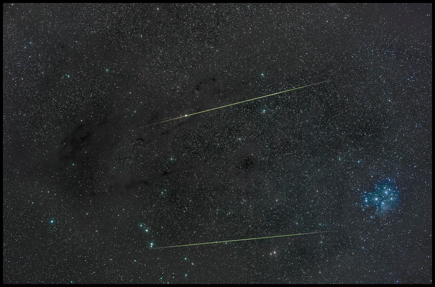 خطّان مخضرّان هما شهابان، على خلفيّة مرصّعة من النجوم تتخلّلها أغبرة عاتمة، بينما يظهر عنقود نجمي مزرقّ على اليمين هو الثريّا.