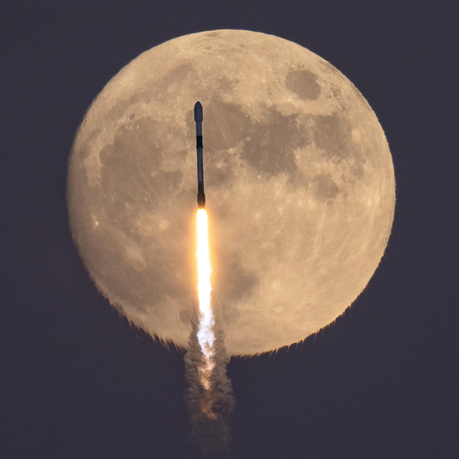قرص قمرٍ مكتمل تقريباً يعبر أمامه صاروخ فالكون وخلفه نيران وأدخنة