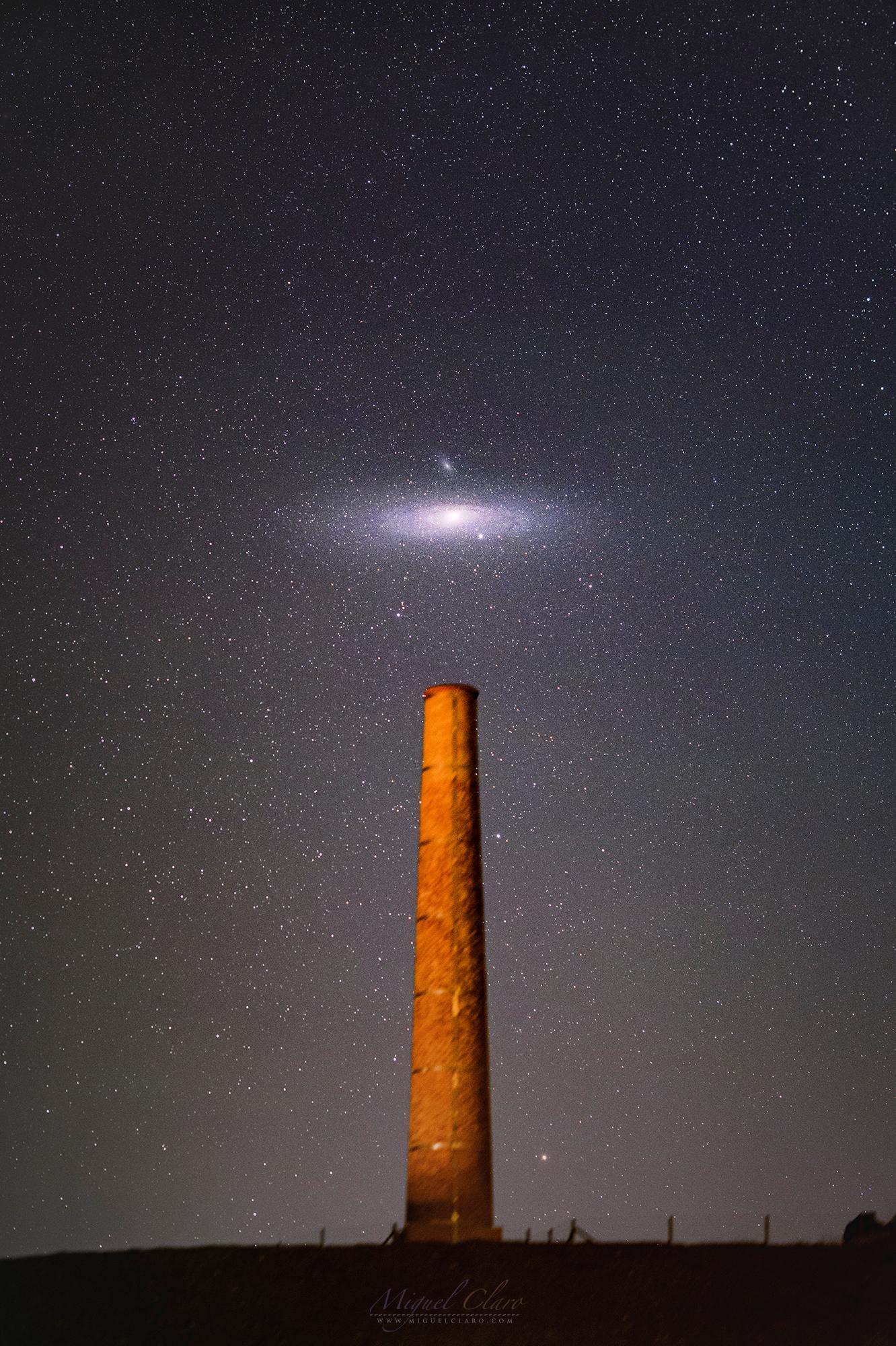 مجرّة حلزونيّة ضخمة في سماء الليل المرصّعة بالنجوم تتموضع مباشرة فوق مدخنة طويلة.