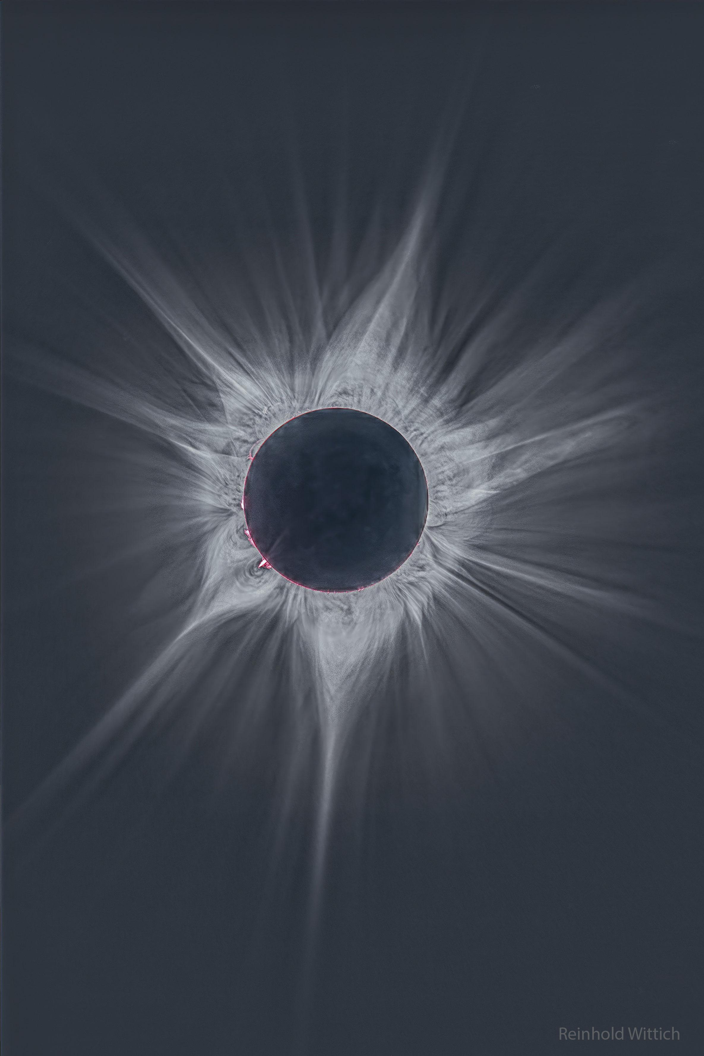 صورة عميقة للإكليل المحيط بالشمس خلال كسوف نيسان 2023 الكلّي. القرص المركزي مظلم بينما نرى العديد من الأشعّة الساطعة والمعقّدة تمتدّ باتّجاه الخارج. تمكن رؤية بعض الخيوط الورديّة الحارّة حول حافّة الشمس مباشرة.
