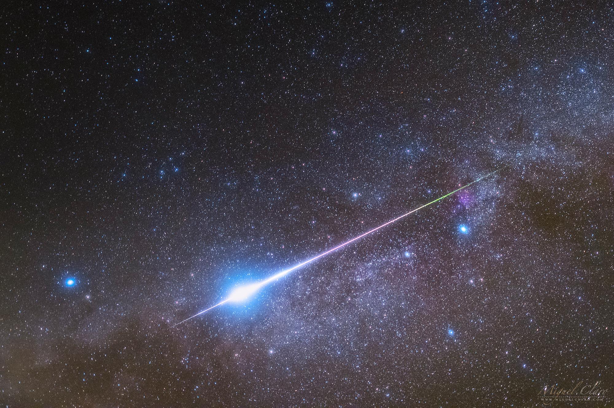 شهاب برشاوي ساطع يخطّ على امتداد مجرّة درب التبّانة من اليمين إلى اليسار عبر إطار الصورة وخلفه السماء المرصّعة بالنجوم.