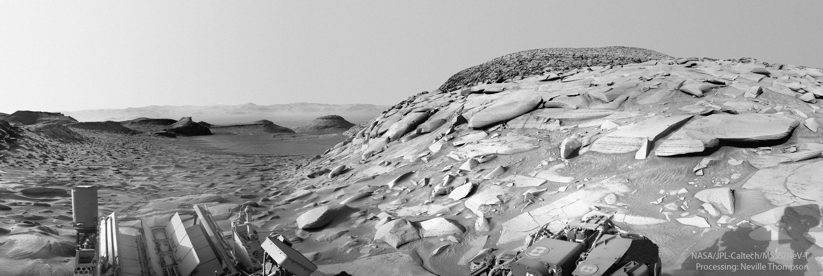 مشهدٌ مُصوّر بالأبيض والأسود للمرّيخ من عربة "الفضول" الجوّالة على المرّيخ. تظهر العديد من الصخور والتلال، مع ظهور تلّة يميناً تحتوي على العديد من الصخور المُسطّحة على نحوٍ غير اعتياديّ.