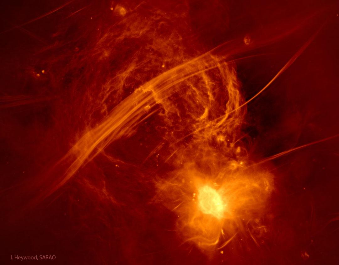 صورة راديويّة حمراء بلون أصفر مُزيّف لمركزنا المجرّيّ تُظهِر أقواساً صفراء باعثة للأشعّة الراديويّة فوق خطوط وشرنقة ساطعة تحتوي على الثقب الأسود المركزيّ لمجرّتنا.