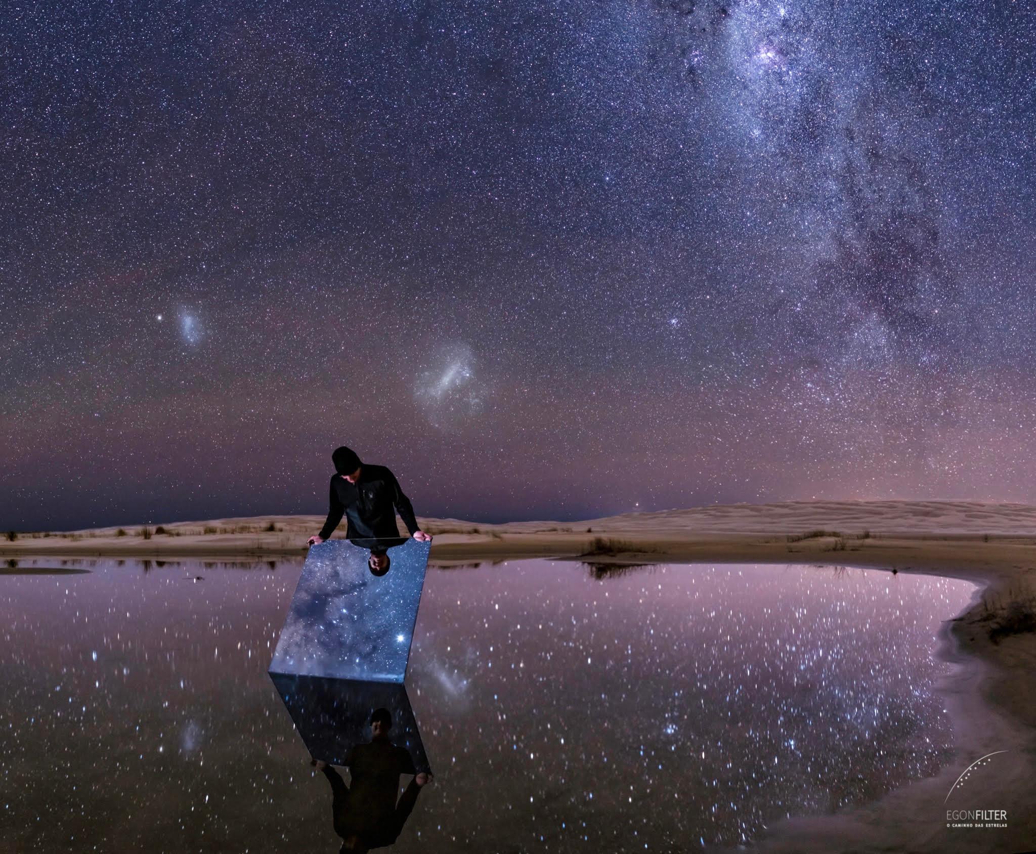 تُظهر الصورة سماءً ليلية صافية من البرازيل والتي تنعكس ليس فقط على الماء الراكدة، بل أيضاً على مرآة يحملها شخص ما. 