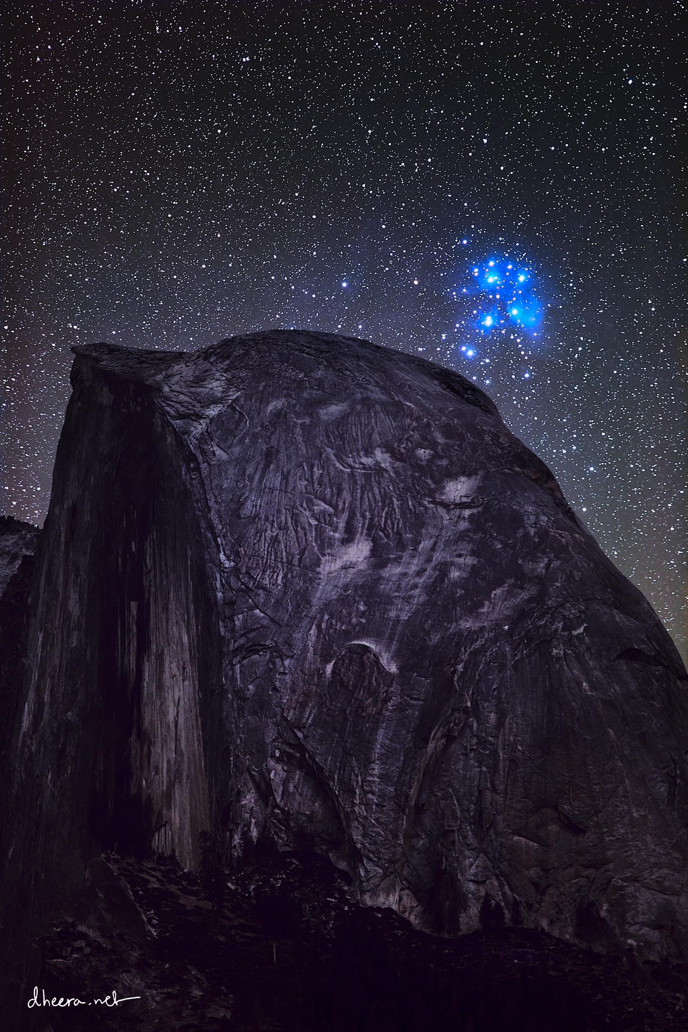 مرتفع صخري وخلفه السماء التي تتناثر فيها النجوم ويزيّنها فوقه تماماً عنقود الثريّا النجمي بنجومه الزرقاء