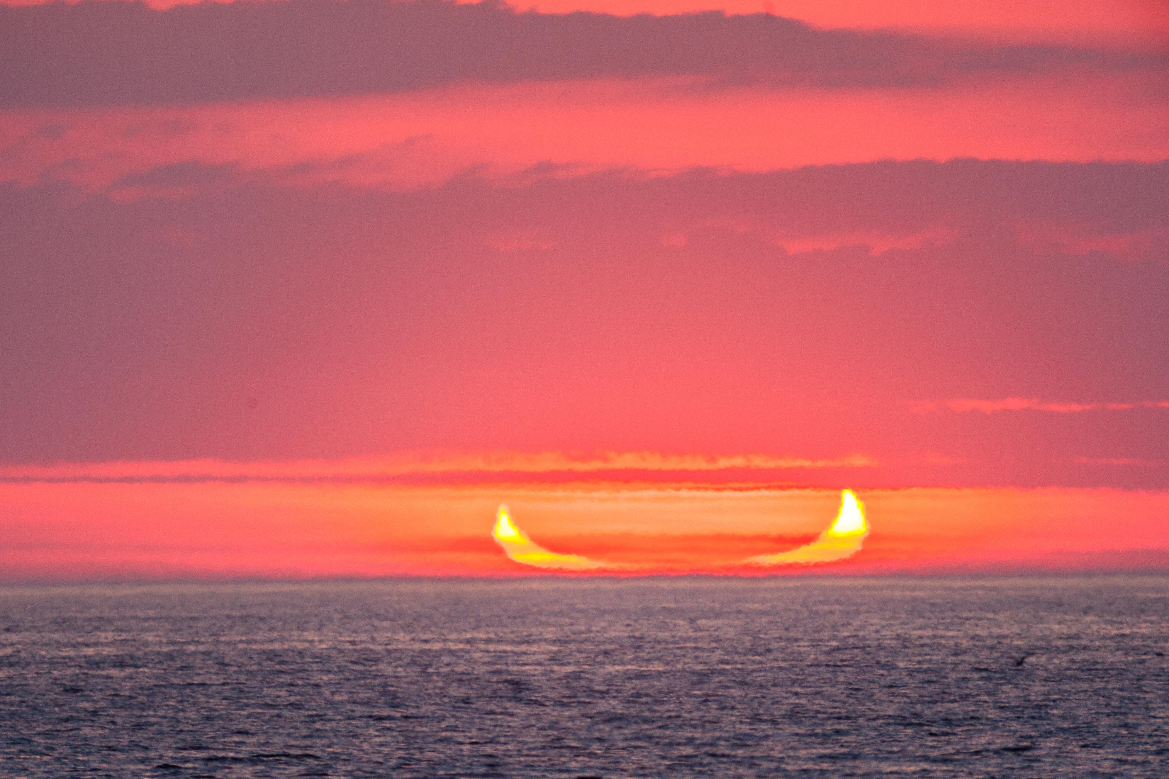 صورة لشروق شمسٍ مكسوفة جزئيّاً عند الأفق على البحر، حيث تظهر كهلالٍ مفتوح باتّجاه الأعلى يمكن تشبيهه بقارب أو قرون.