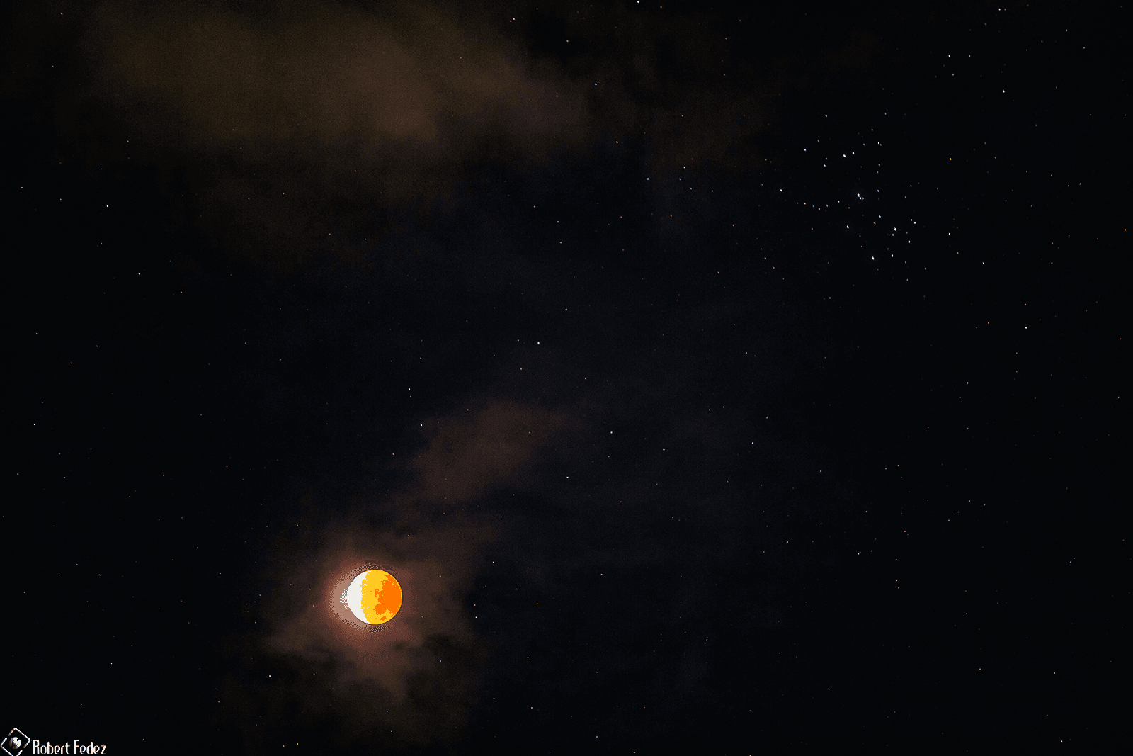 قمر مخسوف كلّيّاً تقريباً يظهر بلون محمرّ في سماءٍ تتخلّلها بعض السحب وترصّعها الكثير من النجوم من بينها نجوم عنقود الثريّا.
