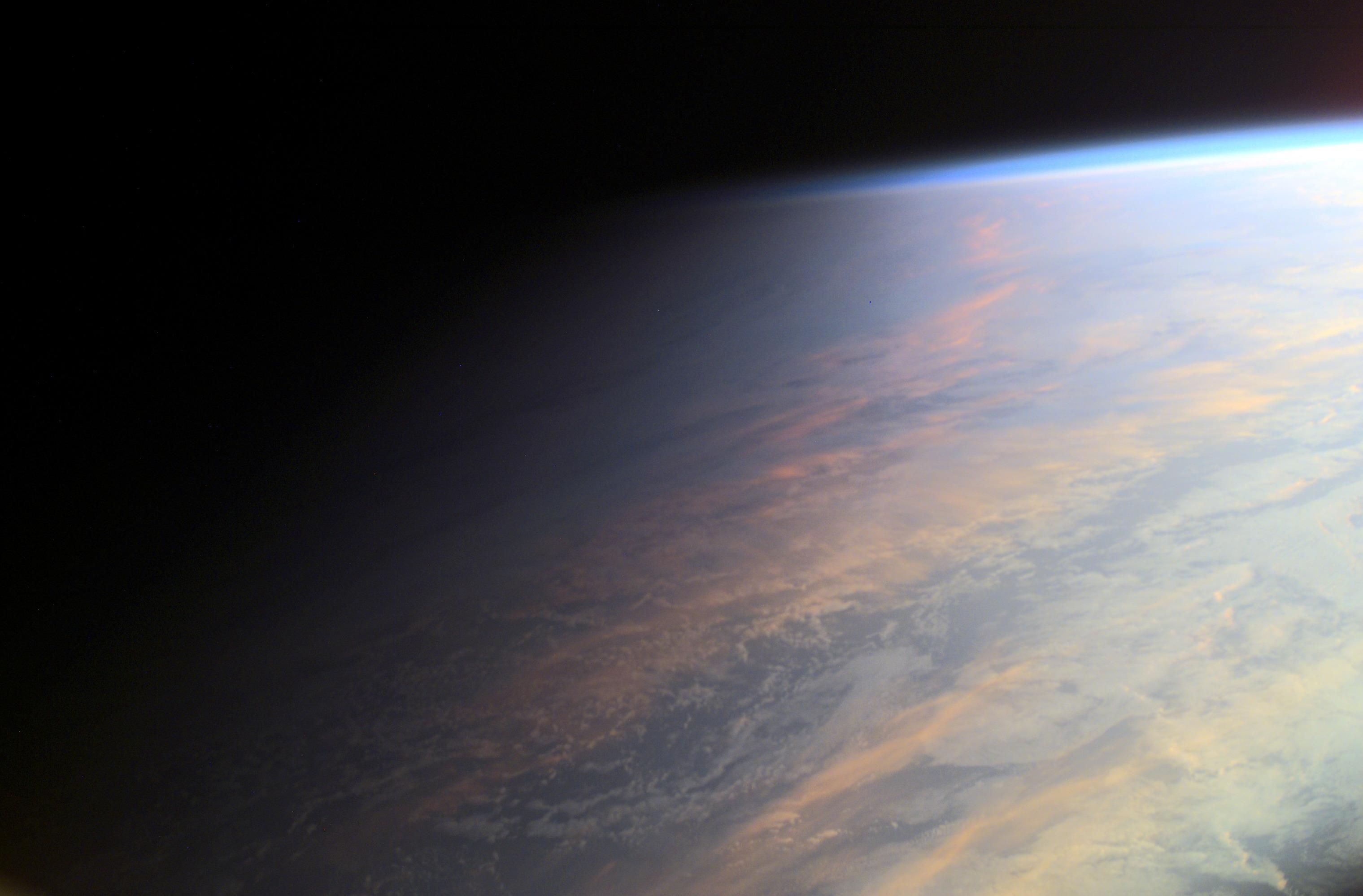 صورة لجزء من الأرض من محطّة الفضاء الدولية يظهر فيها التدرّج بين النهار والليل فوق المحيط، حيث تظهر بعض السحب والتي يعكس بعضها ضوء الشمس المحمرّ، كما تظهر طبقة واضحة عالية الإرتفاع على امتداد الحافّة العليا للجانب النهاري، تقوم بتشتيت ضوء الشمس الأزرق وتتلاشى في سواد الفضاء الغامر.