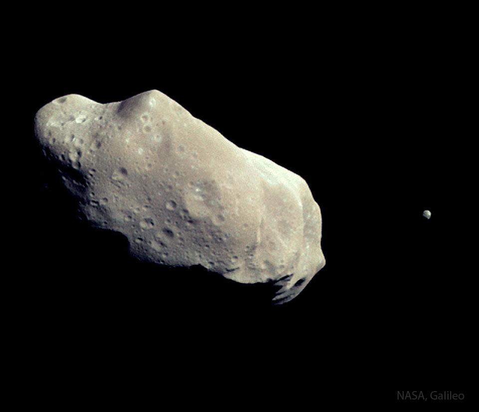 كويكبان أحدهما كبير، متطاول ومليء بالفوّهات يساراً، والآخر أصغر بكثير في أقصى اليمين.