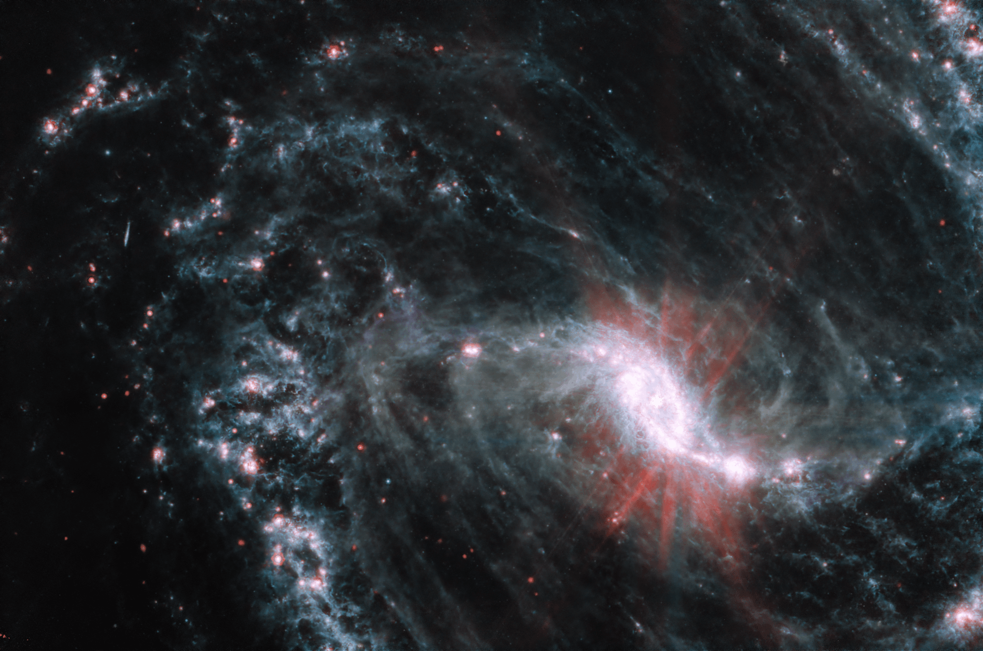 مجرّة حلزونيّة ضلعيّة تظهر بضوء تحت أحمر حيث يظهر مركزّ مشع ساطع وحوله دوّامات من الخيوط والحاضنات النجميّة الورديّة على ما يبدو