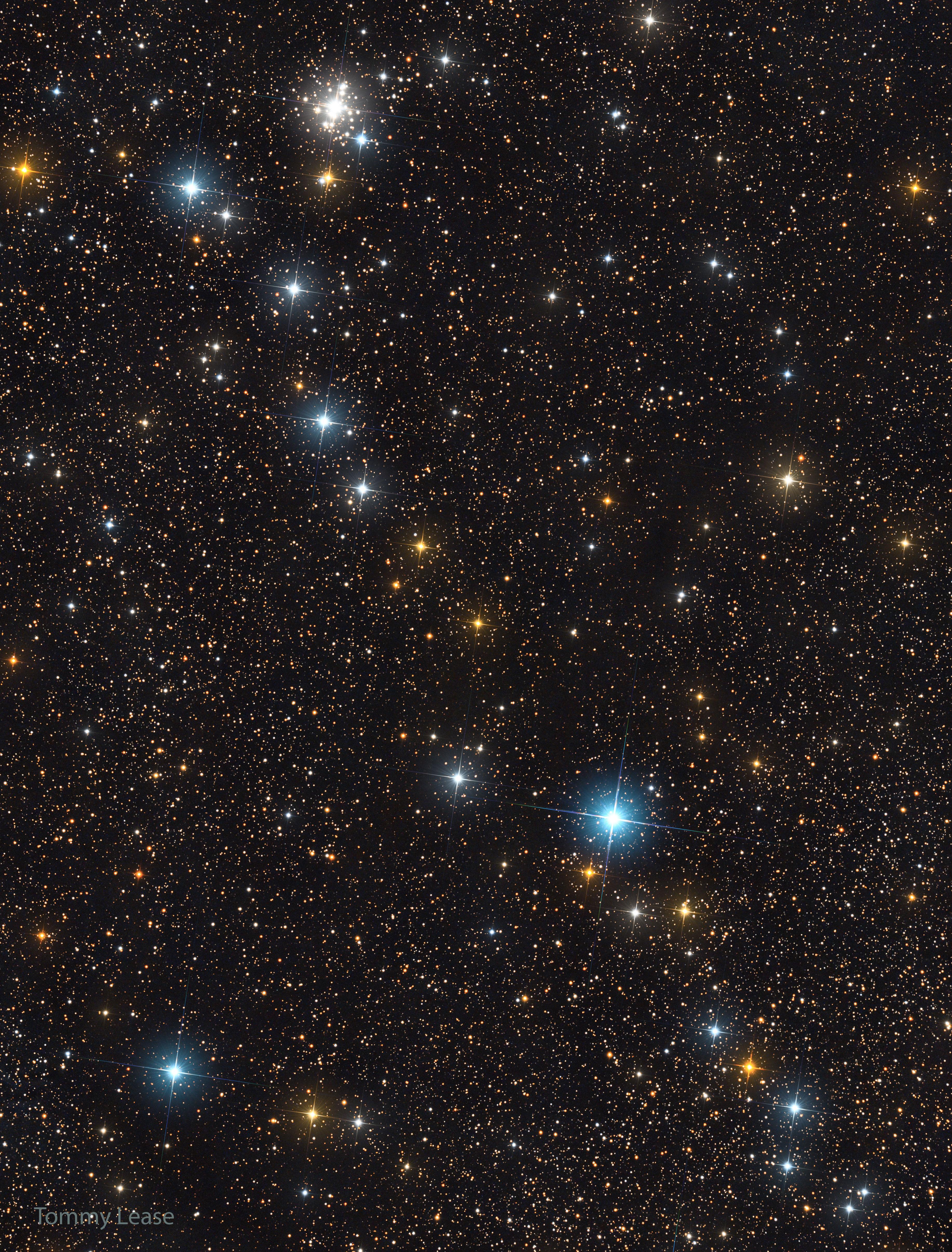 خطّ من النجوم الساطعة المنثورة قُطريّاً عبر حقلٍ من النجوم الأكثر خفوتاً. يظهر عنقود نجمي قرب أعلى اليسار أيضاً