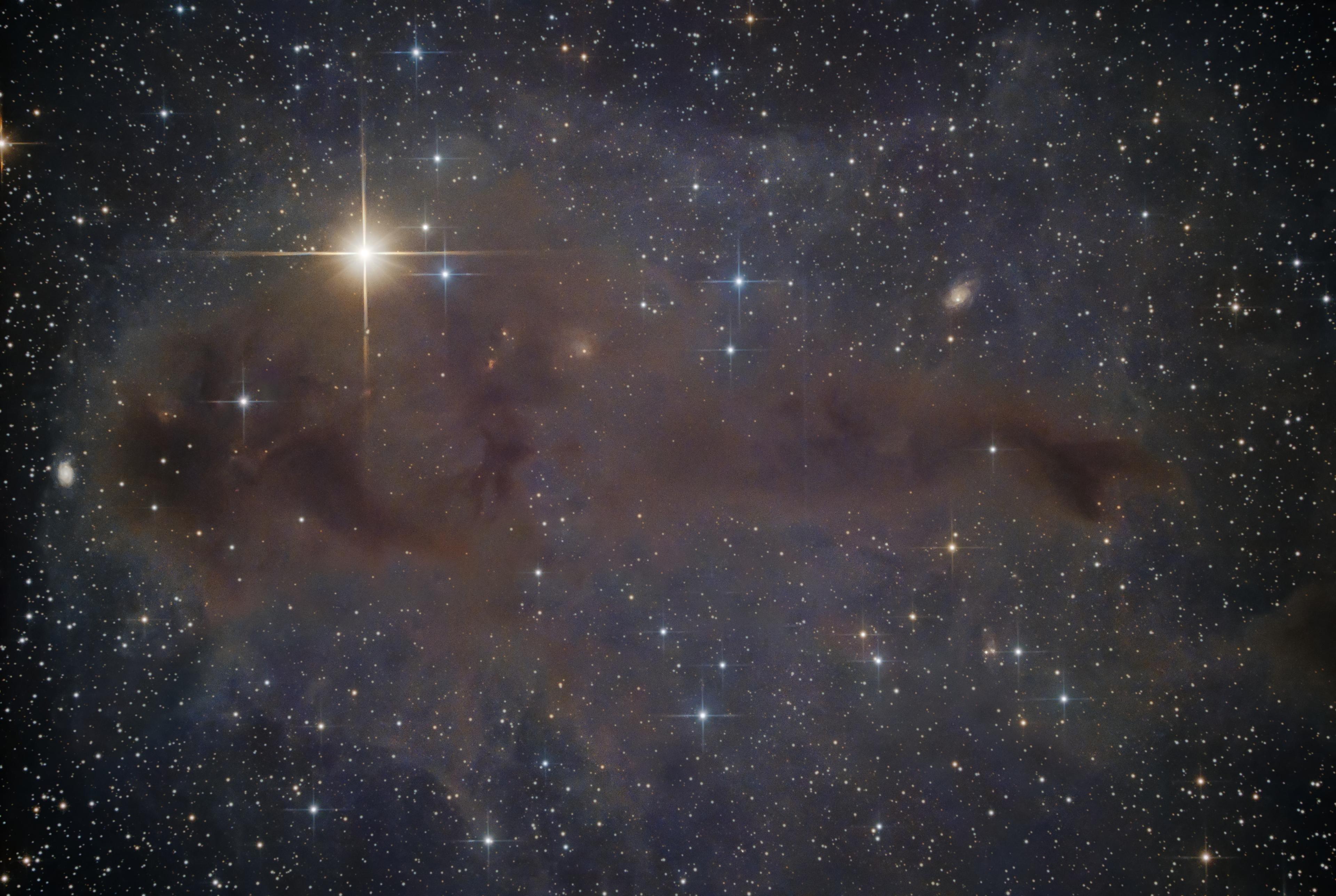 صورة لسحابة بينجمية جزيئية مغبرة في الفضاء العميق تحوي نجوم حديثة التشكل وأمامها نجوم ساطعة مدببة وفي الخلفية بعض المجرات السحيقة.