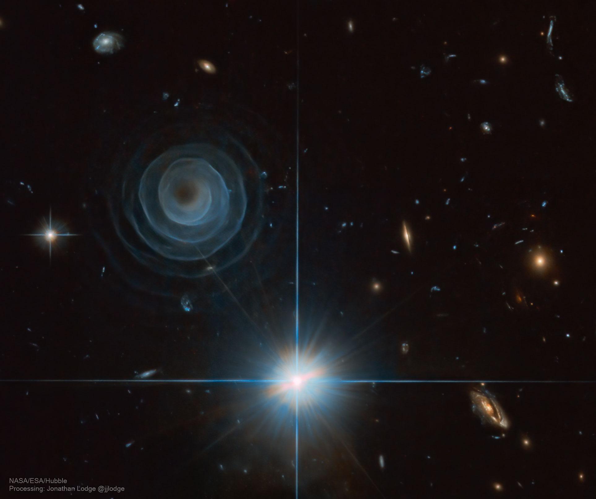 صورة للفضاء العميق تظهر بنية لولبية كطبقات متراكبة حول مركز، حيث تصبح أكثر شفافية باتّجاه الخارج، مع ظهور العديد من النجوم إضافة لمجرات الخلقية