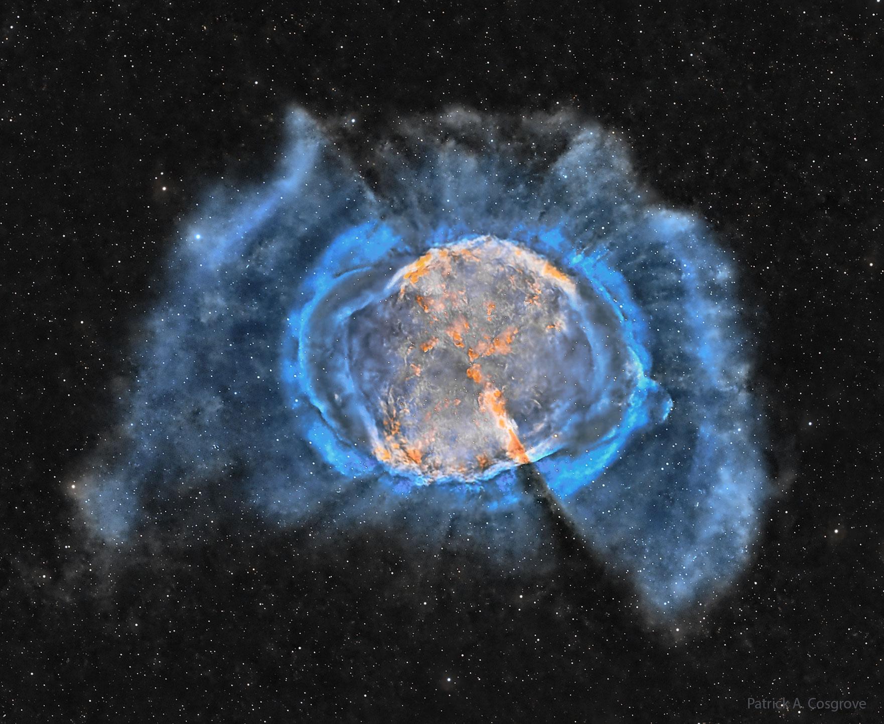 سحابة غاز بينجمي متوسّعة مع داخل برتقاليّ وخيوط زرقاء خارجيّة. تُرى العديد من النجوم في الخلفيّة المُظلمة.