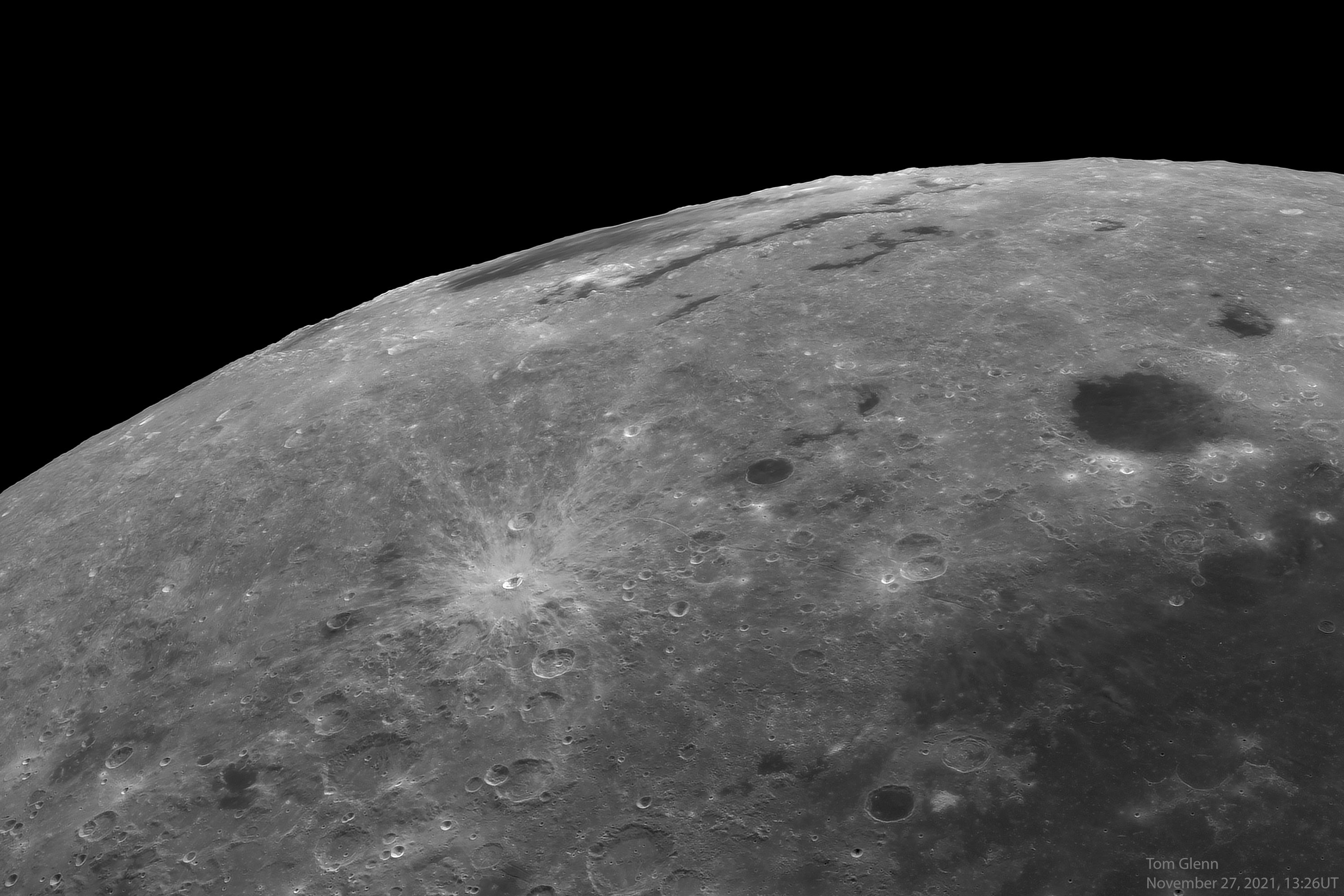 صورة مقرّبة لجزء من سطح القمر تظهر في منتصفه حفرة صدميّة صغيرة نسبيّاً ذات أشعّة بينما يظهر حوض صدمي يظهر مقصَّراً على امتداد الحافة في أعلى المنتصف