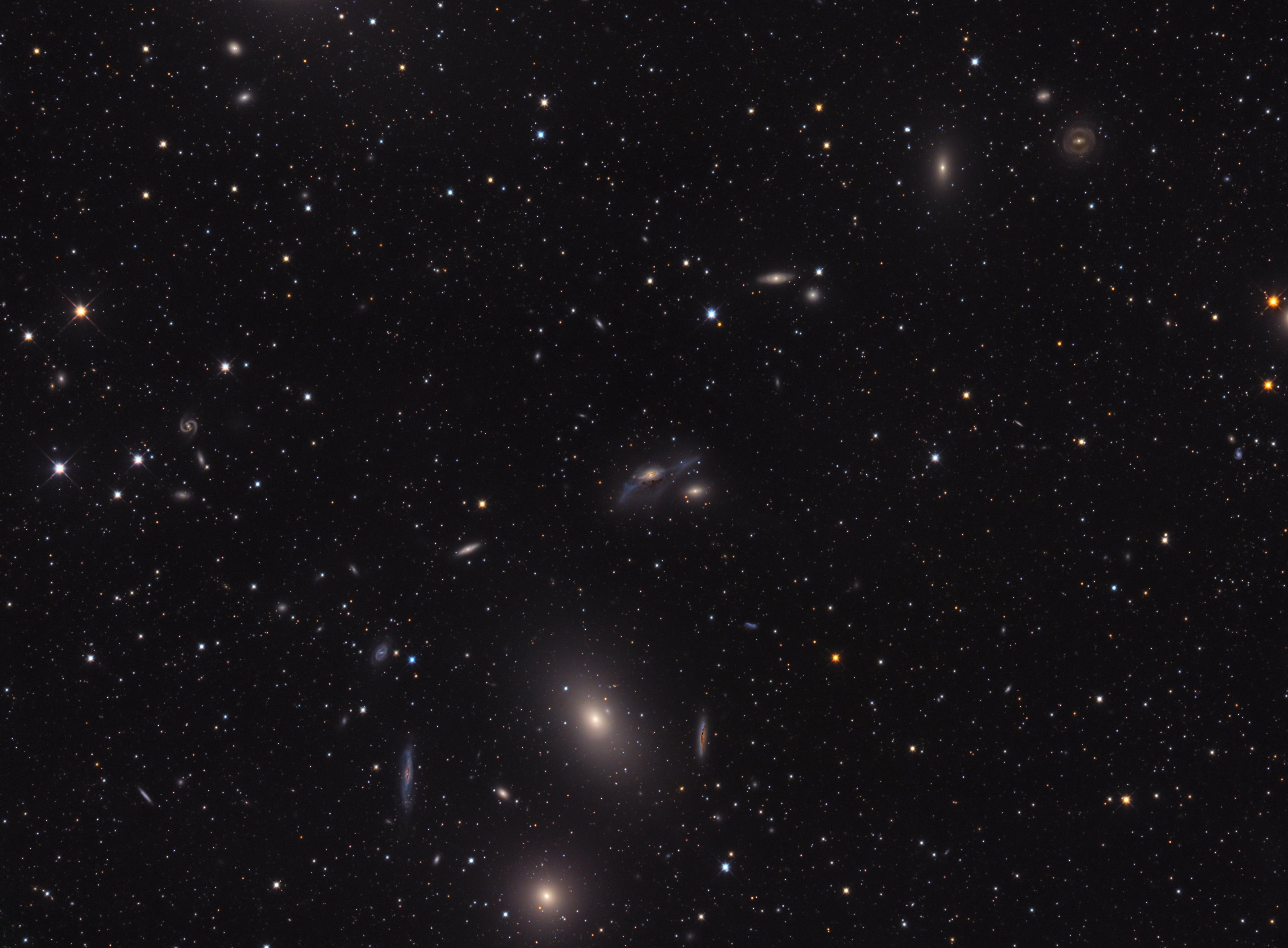 صورة تلسكوبيّة مزدانة بالنجوم للفضاء العميق يمكن فيها تمييز سلسلة من المجرّات التي تمتد من أسفل المركز حيث تظهر مجرّتان ساطعتان باتّجاه الأعلى واليمين. يمكن تمييز عدّة أنواع من المجرّات فبعضها حلزونيّة وبعضها إهليلجيّة كما تظهر واحدة غير منتظمة في وسط الصورة.