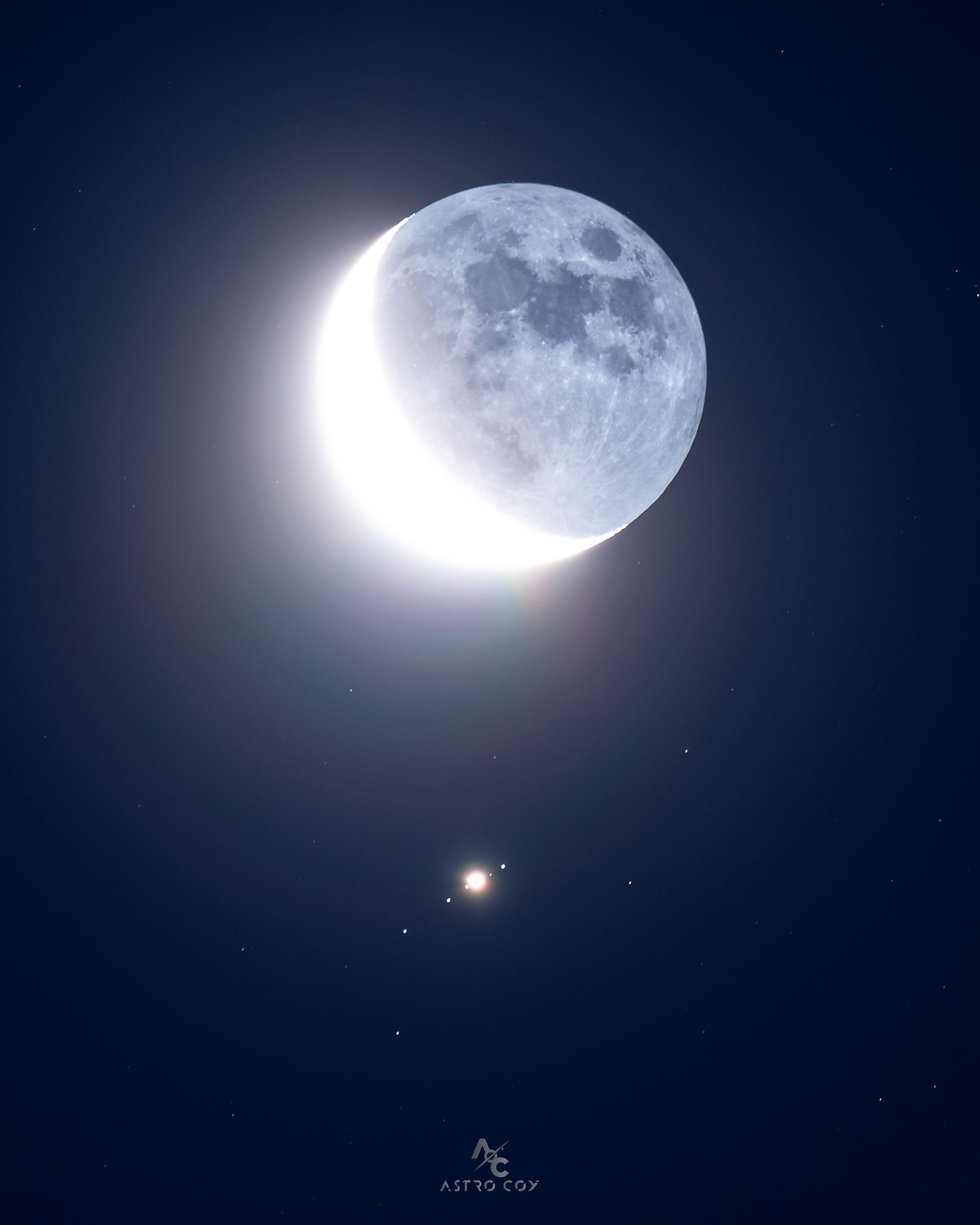 يُرى قمر الأرض، في طور الهلال، فوق مركز الصورة تماماً. في الأسفل تماماً بقعةٌ ساطعة مُحاطة بأربع بُقَعٍ أُخرى، جميعها في صفّ، وهي جميعها من أقمار المُشتري.