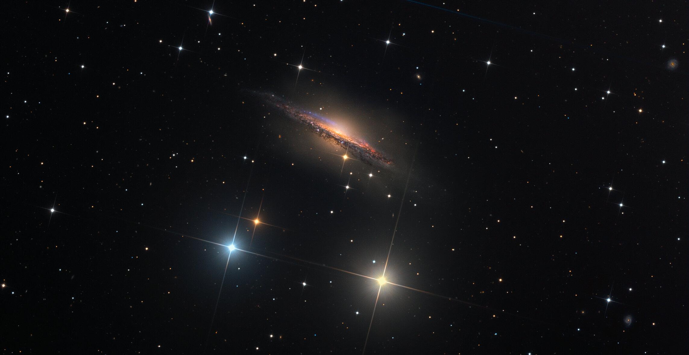 المجرة الحلزونية إن‌جي‌سي 1055 والتي تظهر لنا من جهة حافّتها. تظهر في الصورة نجوم ملونة ومدببة، كما تحتوي على مناطق ورديّة متناثرة بين ممرات الغبار الملتوية على امتداد القرص الرفيع للمجرة البعيدة. تظهر كذلك المزيد من المجرات الخلفية البعيدة الظاهرة بشكل سطحي بسيط. تكشف الصورة العميقة كذلك عن هالة صندوقية تمتد كثيراً أعلى وأسفل قرص هذه المجرة.
