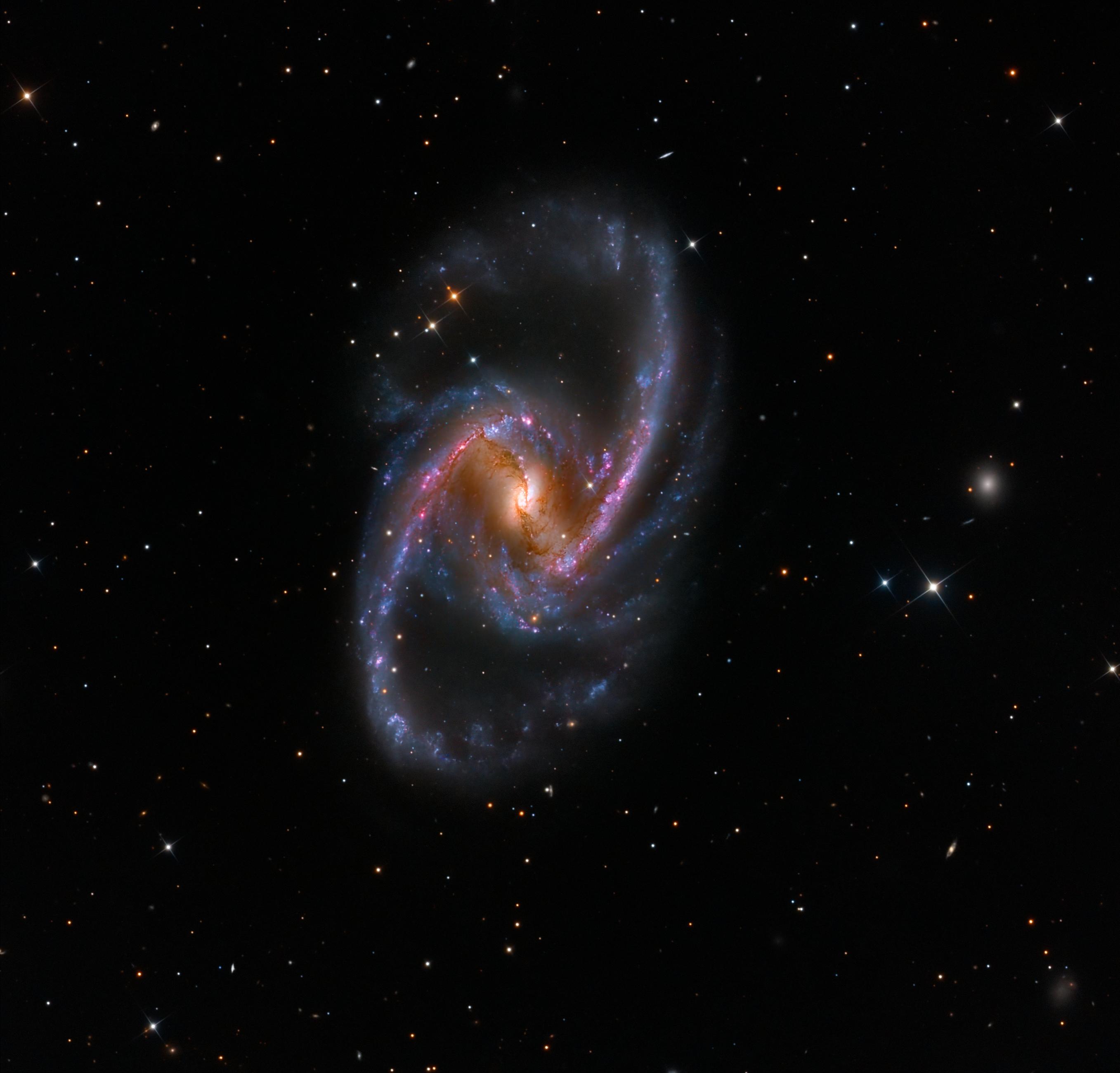 مجرّة "إن‌جي‌سي 1365" الحلزونيّة الضلعيّة مع مناطق تشكّل النجوم المُحمرّة، بالإضافة لممرات الغبار المُعتِم أمام النواة التي يقع ثقبٌ أسودٌ مركزيٌّ عندها.