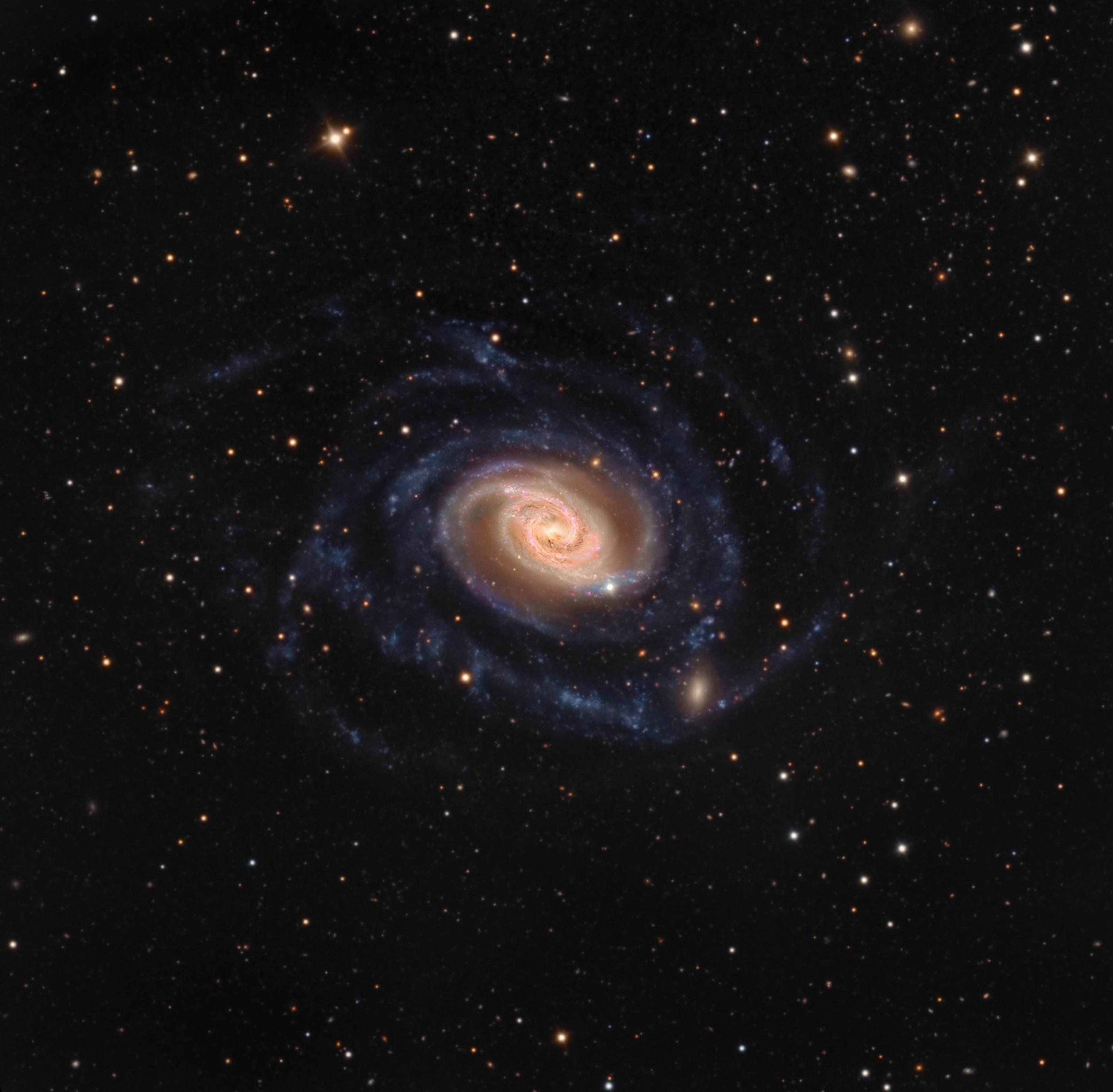 مجرة إن‌جي‌سي 289 الحلزونية بأذرعها الملتفة وقرصها الملوّن مع مجرّة مصاحبة صغيرة زغِبة في الأسفل قرب أحد الأذرع. توجد نجوم مدبّبة في المقدمة.