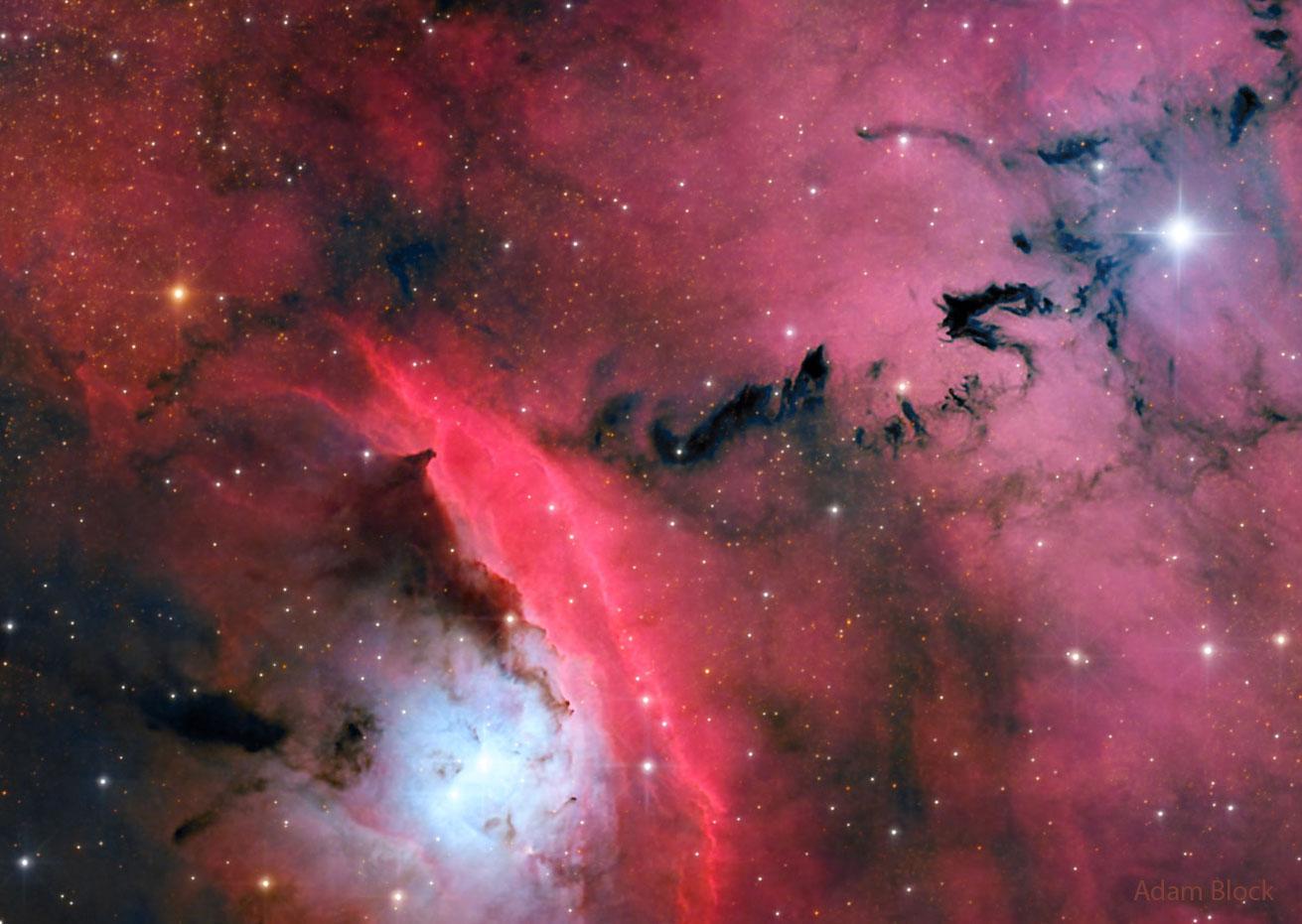 منطقة تشكّل نجومٍ مُزدحمة تُبرزها السُّحُب المُتوهّجة الحمراء والغبار المُظلم ذو الأشكال المُنذِرة بالشؤم.
