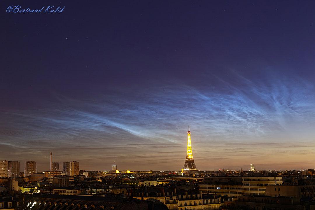 سماء ليل تنساب فيها سحبٌ متألّقة وتحنها برج إيفل ومدينة باريس