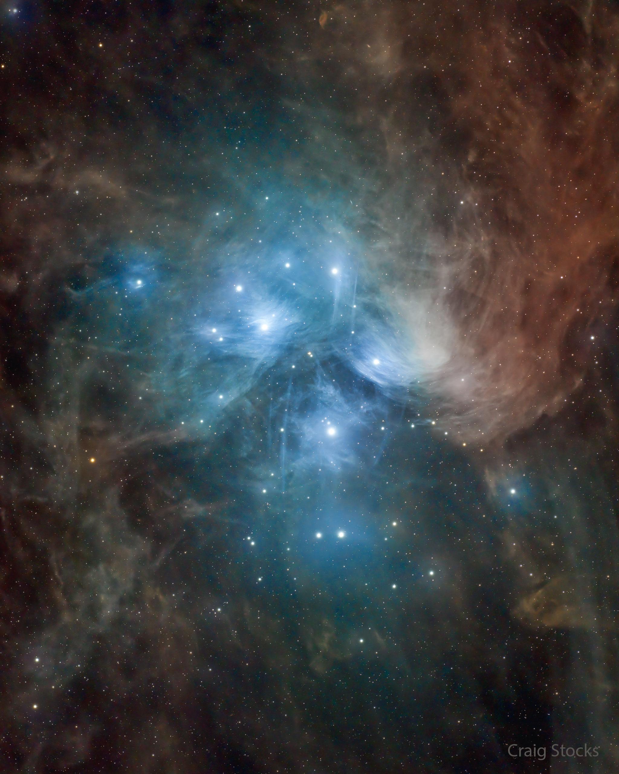 يظهر عنقود نجوم الثُّريّا محاطاً بالغبار. يعكس الغبار قرب النجوم الساطعة الضوءَ الأزرق، لكن الغبار الأبعد يبدو أحمر أكثر.