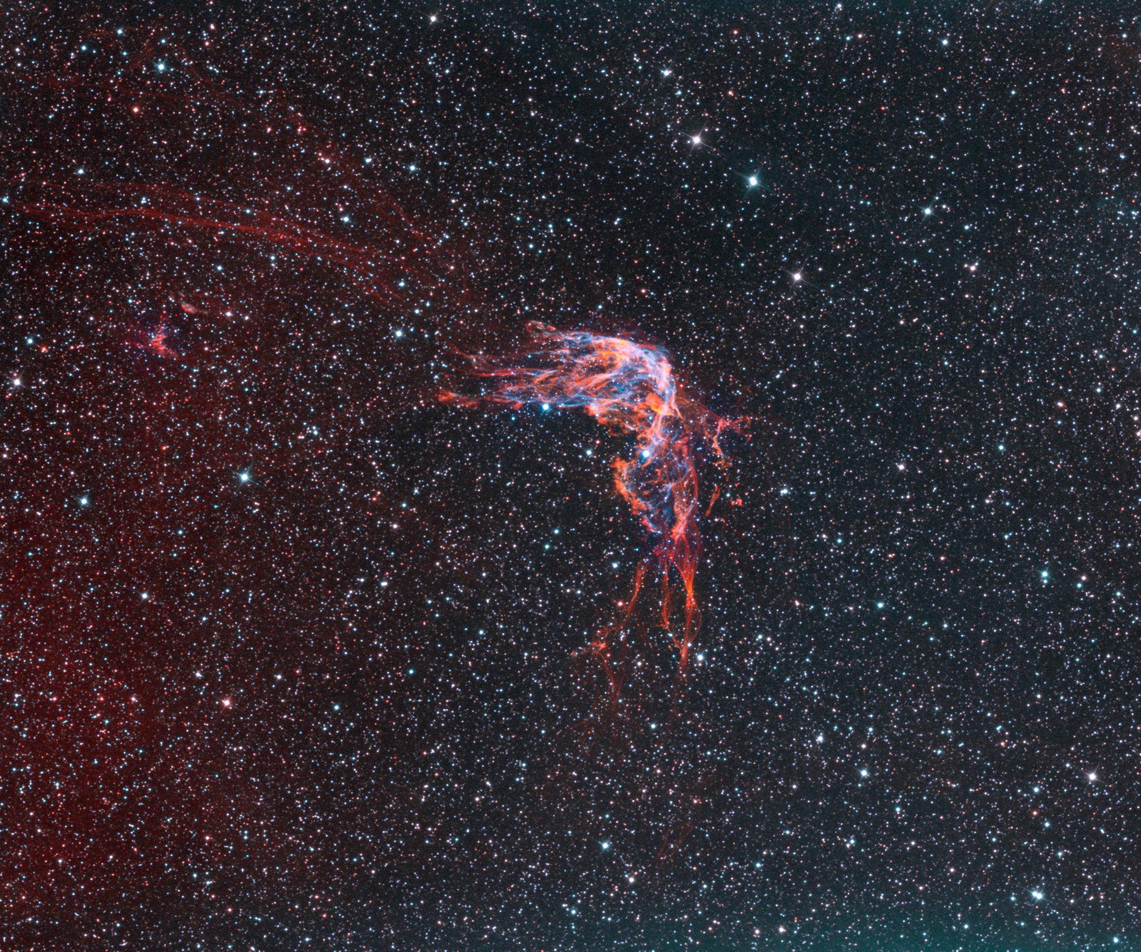 سديم انبعاثي يظهر كشبكة خيوط محمرّة تشوبها بعض الزرقة على خلفية من النجوم