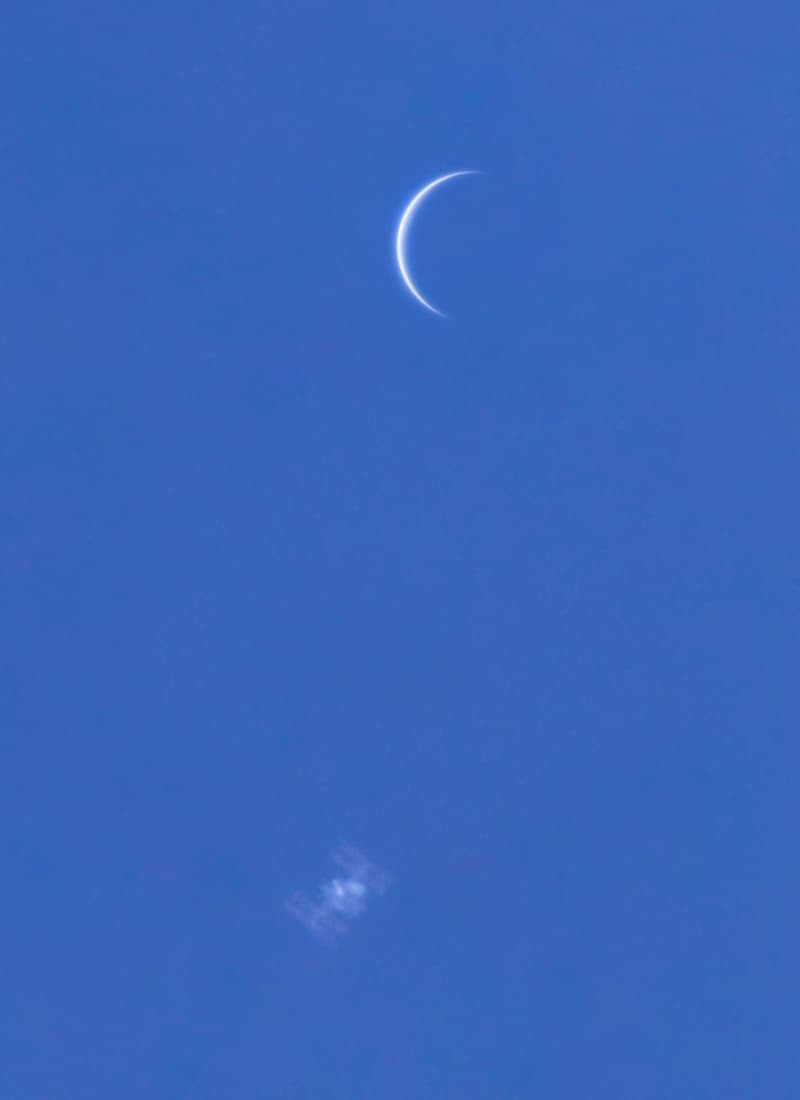 رقعة زرقاء من السماء فيها هلال نحيل هو الزهرة وأسفله شكل باهت هو محطّة الفضاء الدوليّة