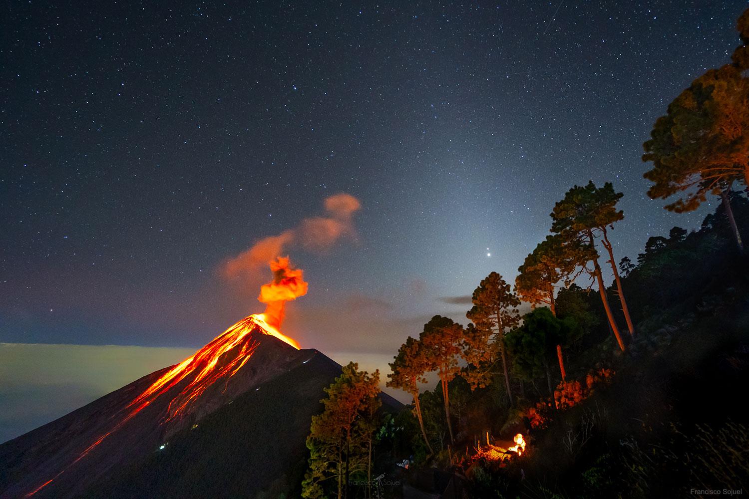 صورة من غواتيمالا تظهر كوكبي المشتري وزحل على يمينها فوق شجرة مباشرة يغمرهما الوهج المنتشر لأنوار السماوات، بينما يظهر على اليسار بركان ثائر