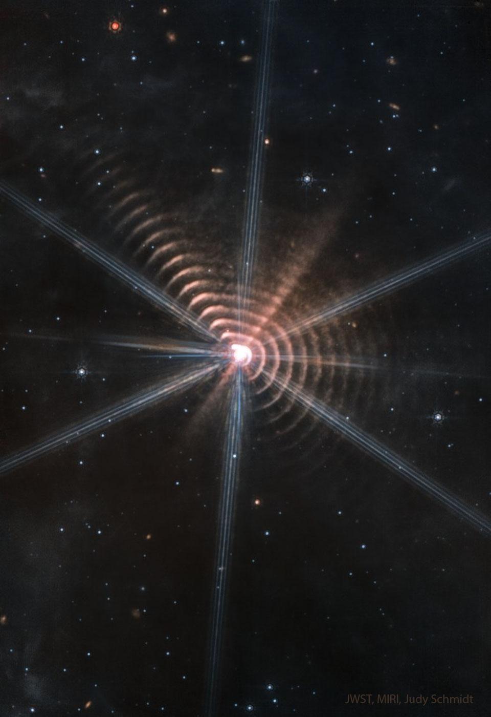 حلقات دائريّة عديدة تحيط بنجم مركزي. تظهر نجوم أخرى في حقل مظلم لولا ذلك