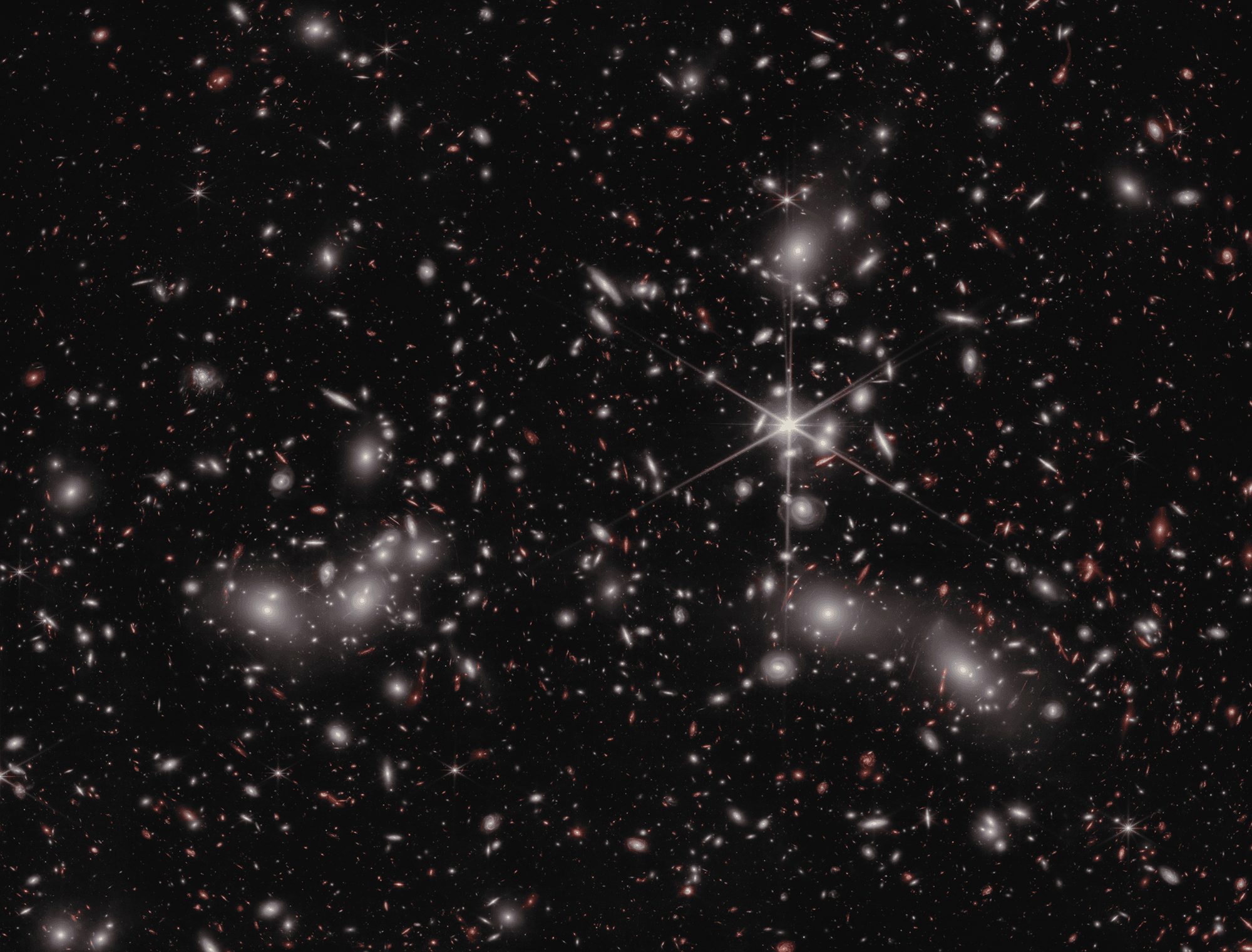 العديد من المجرّات المتناثرة عبر الصورة بعضها أحمر مُعدّس ثقاليّاً في الخلفيّة البعيدة، في حين تظهر بعض نجوم المقدّمة المدبّبة