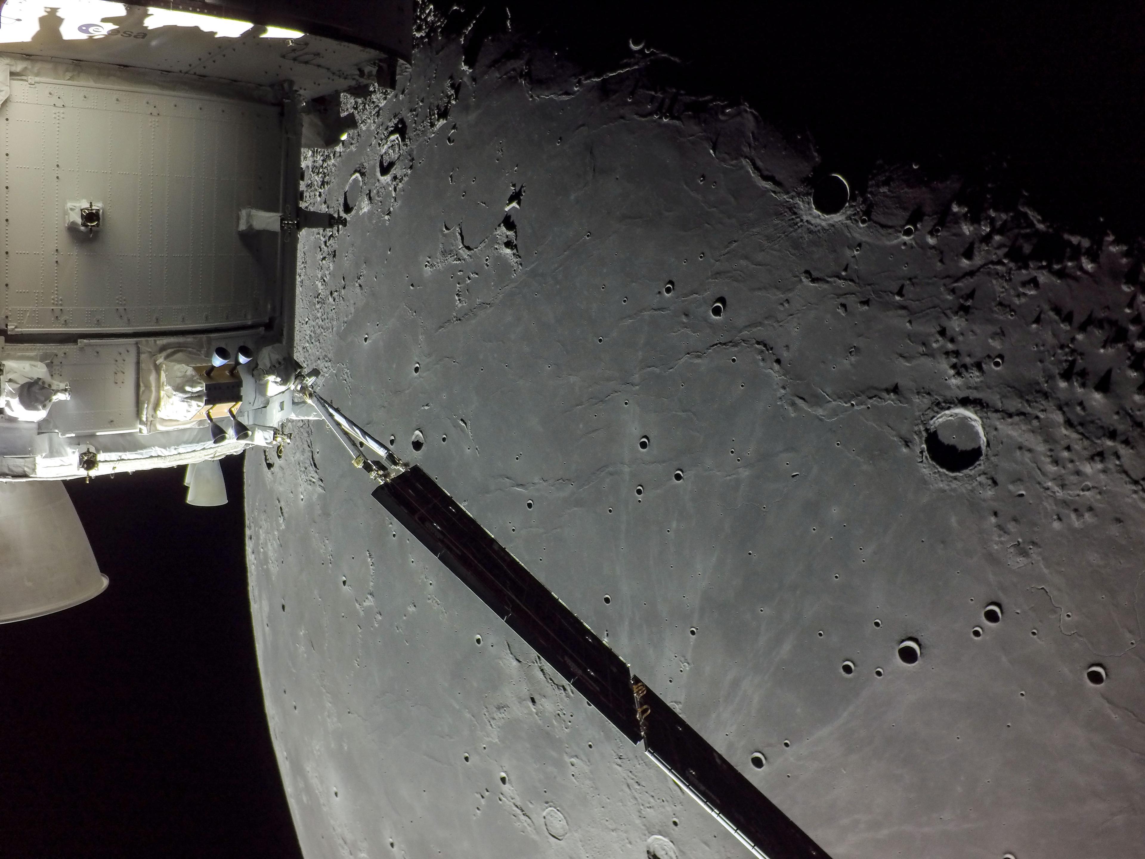 مركبة أورَيون الفضائيّة تمتد منها مصفوفة ألواح شمسيّة ومن تحتها السطح القمري المليء بالفوّهات