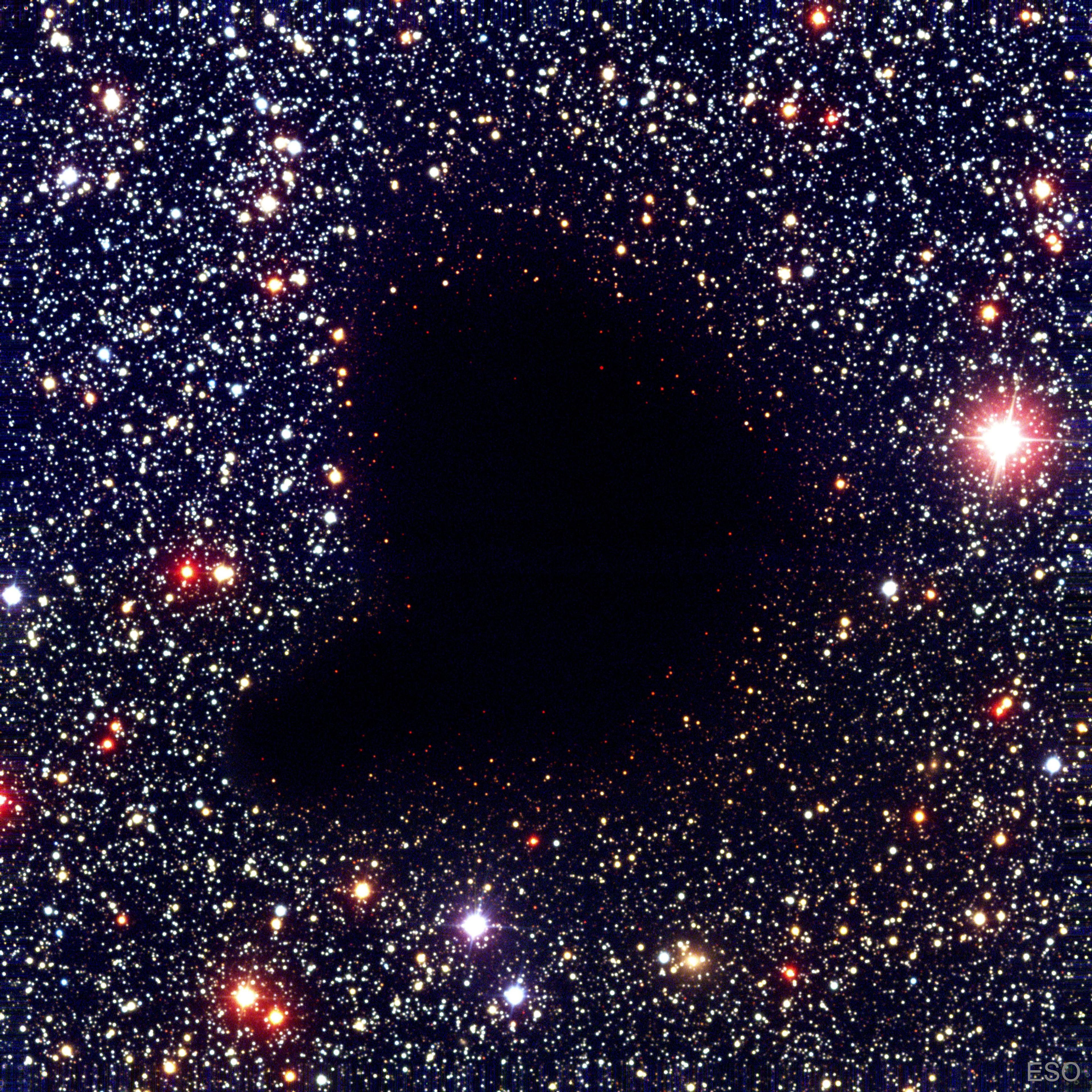 سحابةٌ مُظلِمة على شكل فاصِلة تظهر في منتصف حقلٍ كثيفٍ من النجوم. لا توجد نجومٌ مرئيّة عبر مركز السحابة.