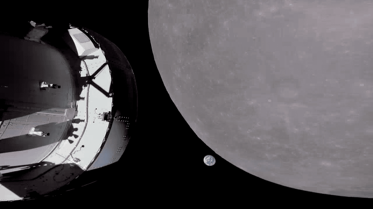 قرص القمر رمادي كبير يغطي نصف الصورة والأرض كرة زرقاء صغيرة بجانب حافّته بينما تظهر أجزاء من مركبة أوريون الفضائيّة على اليسار