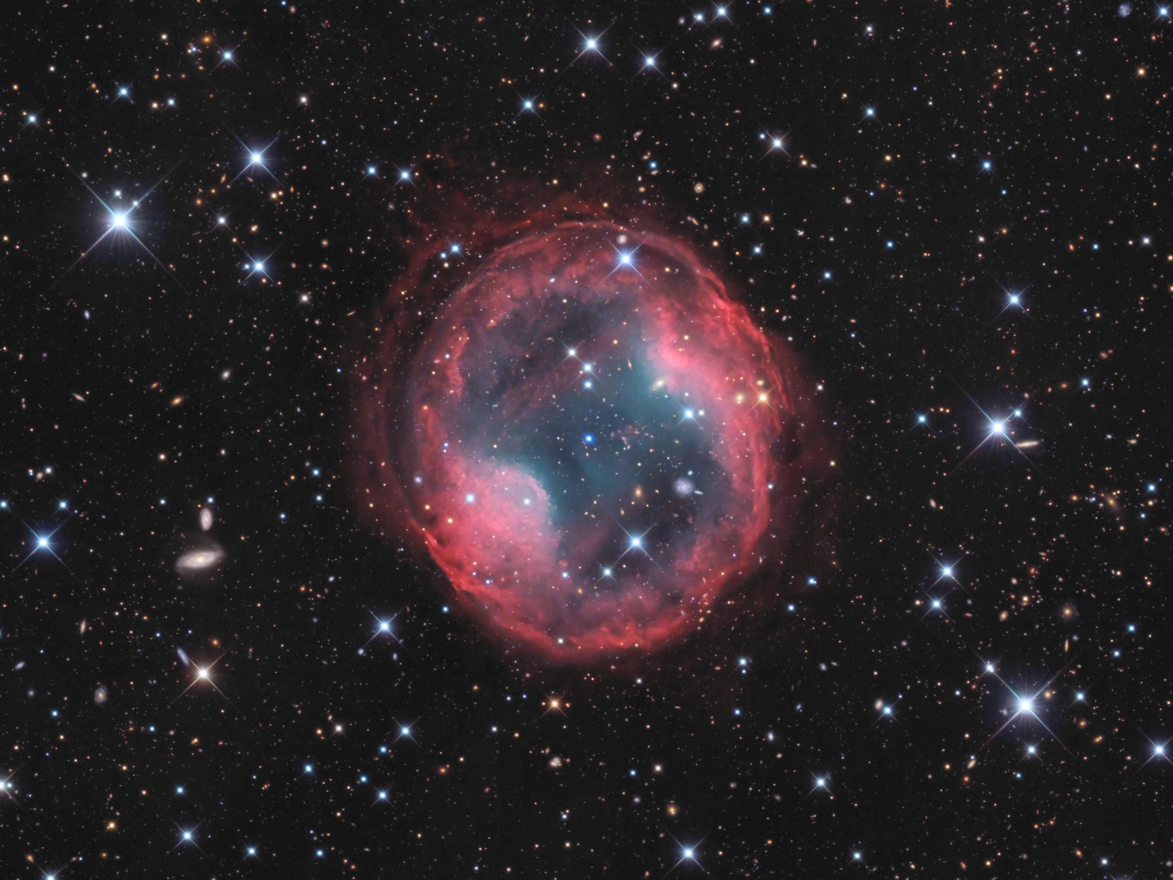 سديم كوكبي يبدو كفقاعة محمرّة تحيط بنجم مركزي مزرق بينما تمتدّ عبر الصورة نجوم بعضها يظهر مدبّباً