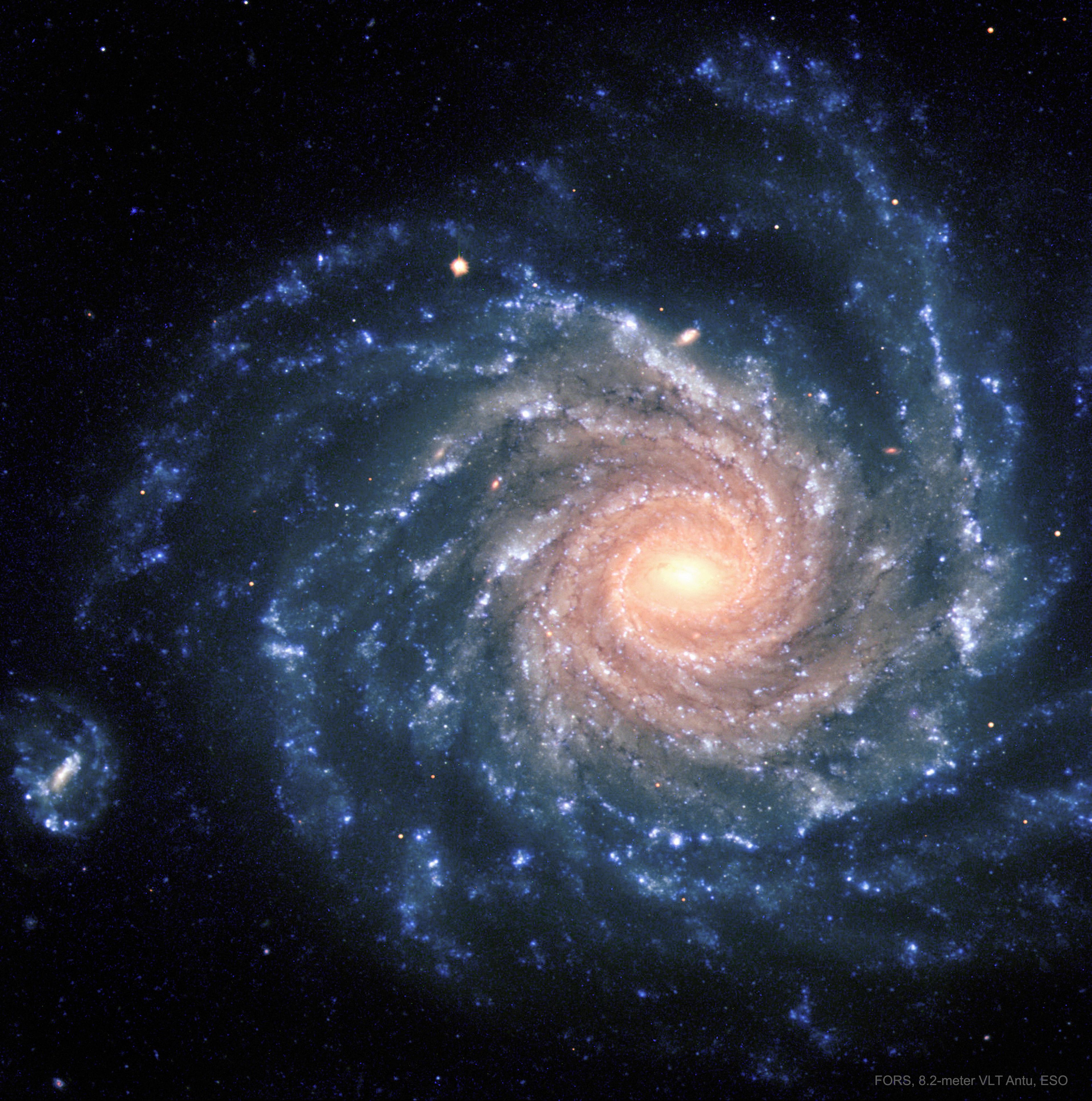 تظهر مجرّة حلزونيّة بأذرع حلزونيّة زرقاء كبيرة ومركزٍ يبدو أكثر صُفرةً.