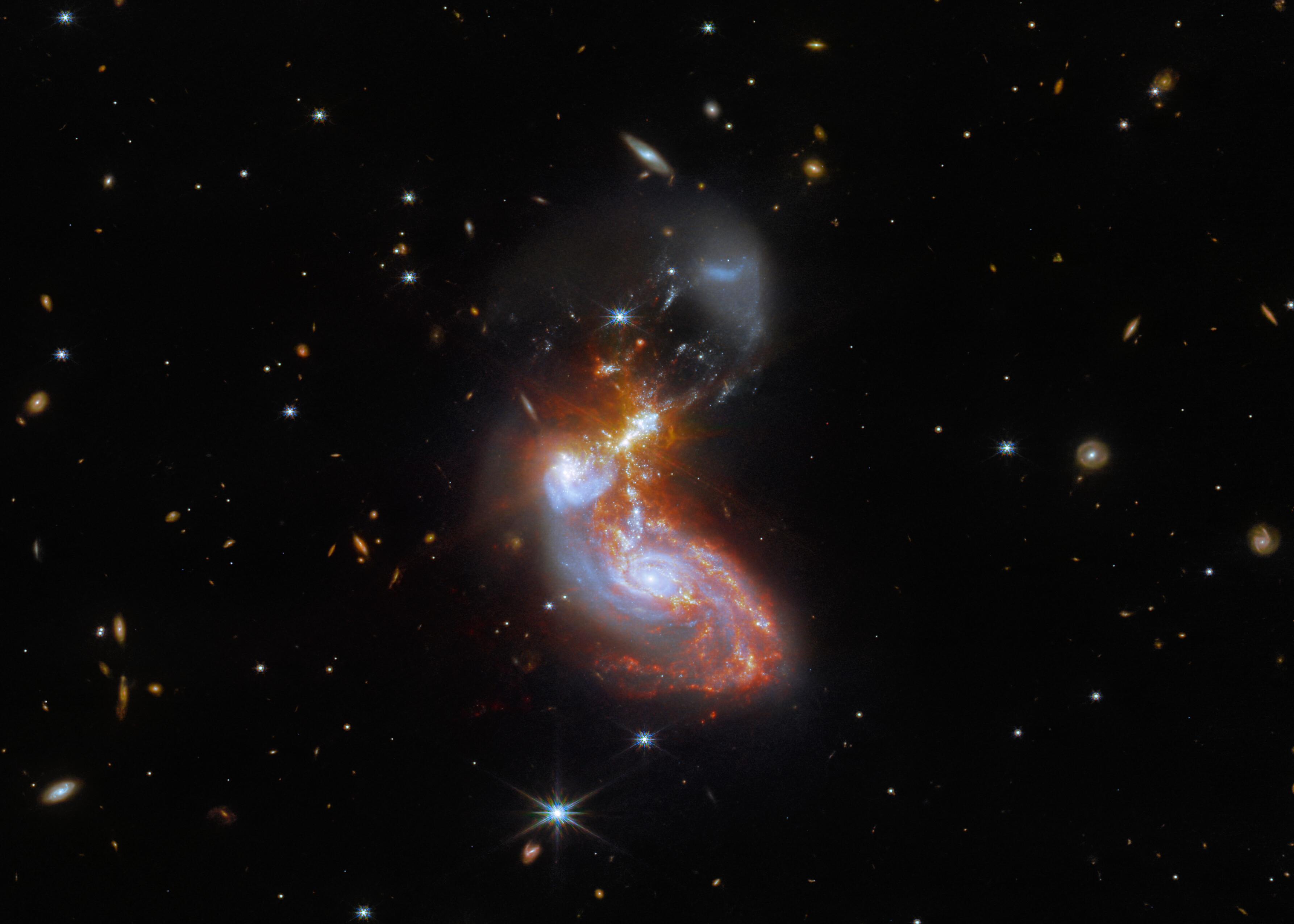 مجرّتان حلزونيّتنان قيد الإندماج وترح حولهم مجرّات أبعد ونجوم مقدّمة