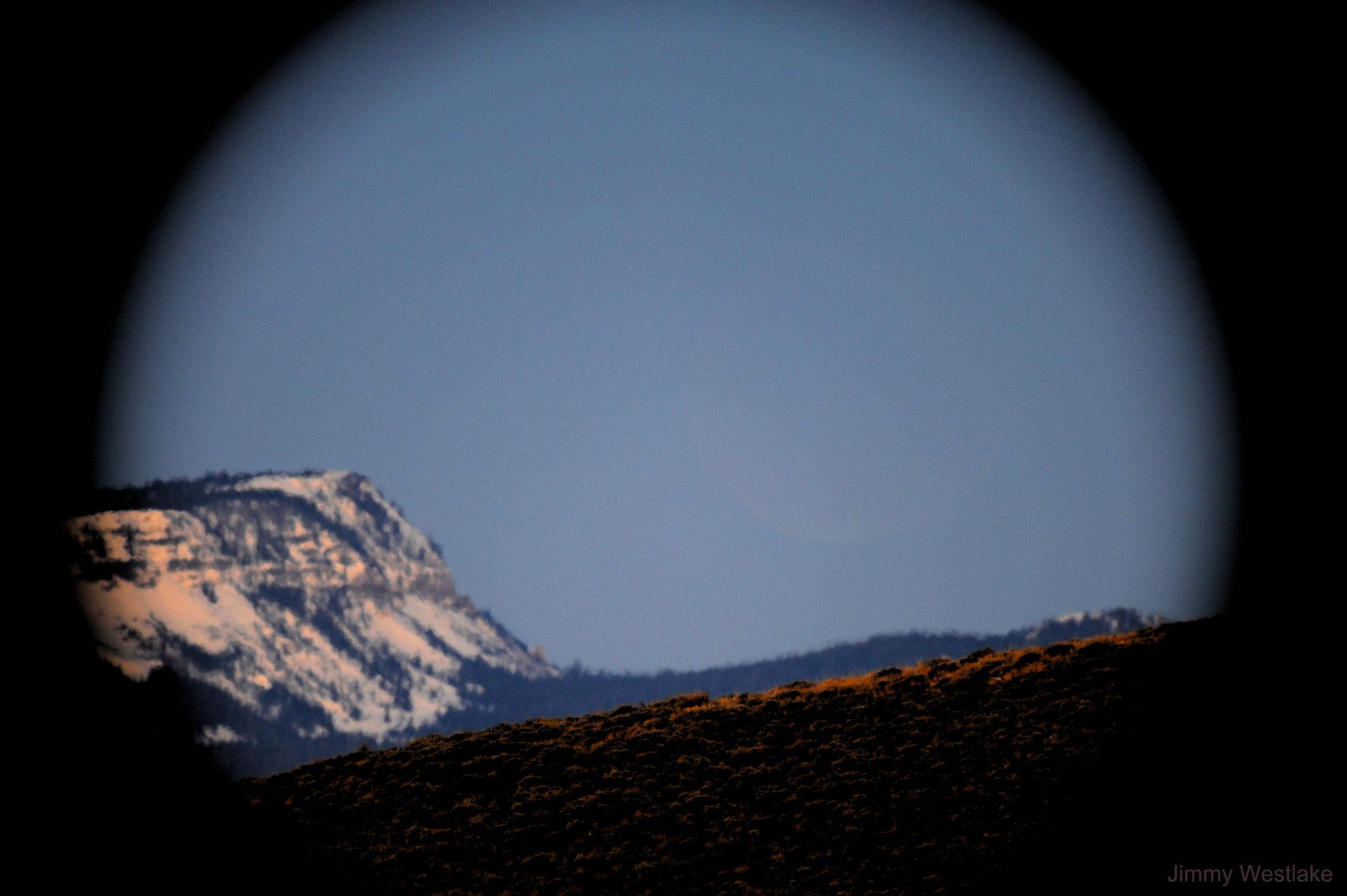 صورة للأفق وبالكاد تمكن رؤية القمر كبدر خافت جدّاً فوق بعض الجبال على خلفيّة السماء الزرقاء.