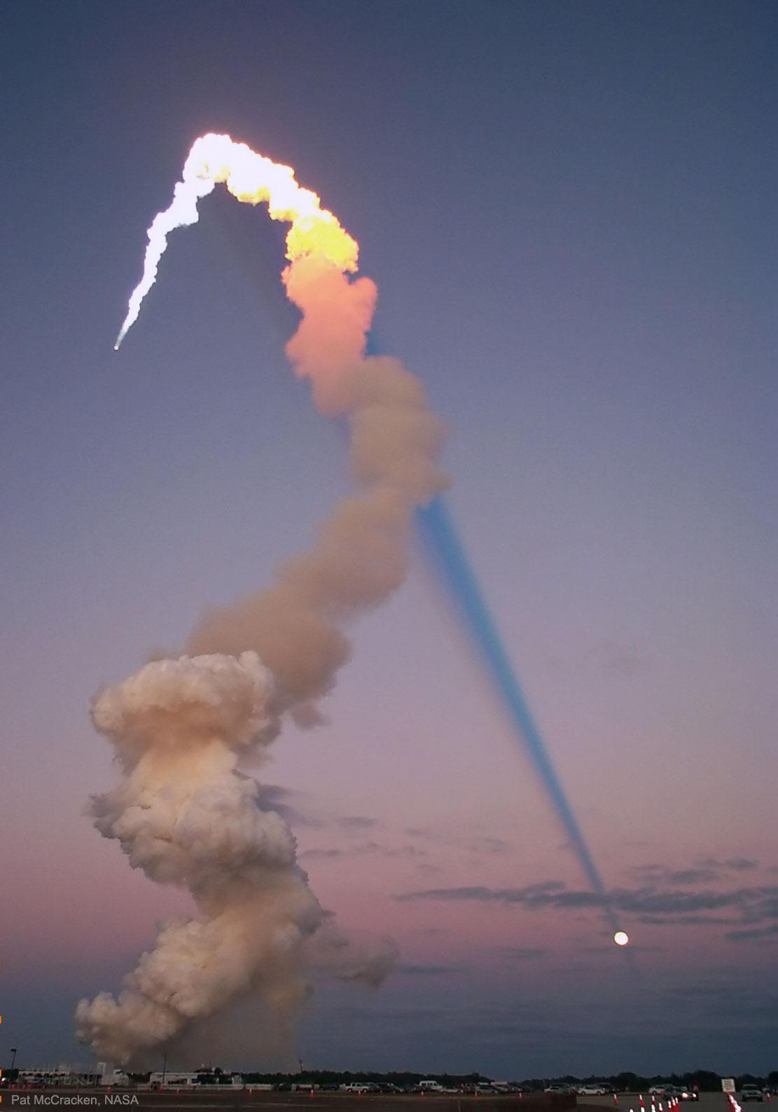 يُرى عمود الدخان الطويل لصاروخٍ مُطلَق على الجانب الأيسر للصورة. يكون الجزء الأعلى من عمود الدخان ساطعاً، بينما الجزء الأسفل بُنّيٌّ دخانيّ. الجزء الساطع من عمود الدخان مُنارٌ بواسطة الشمس ويُلقي ممرّ ظلٍّ طويلاً ومُظلِماً عبر الصورة. يبدو الظلّ أنه ينتهي على القمر المُكتَمِل.