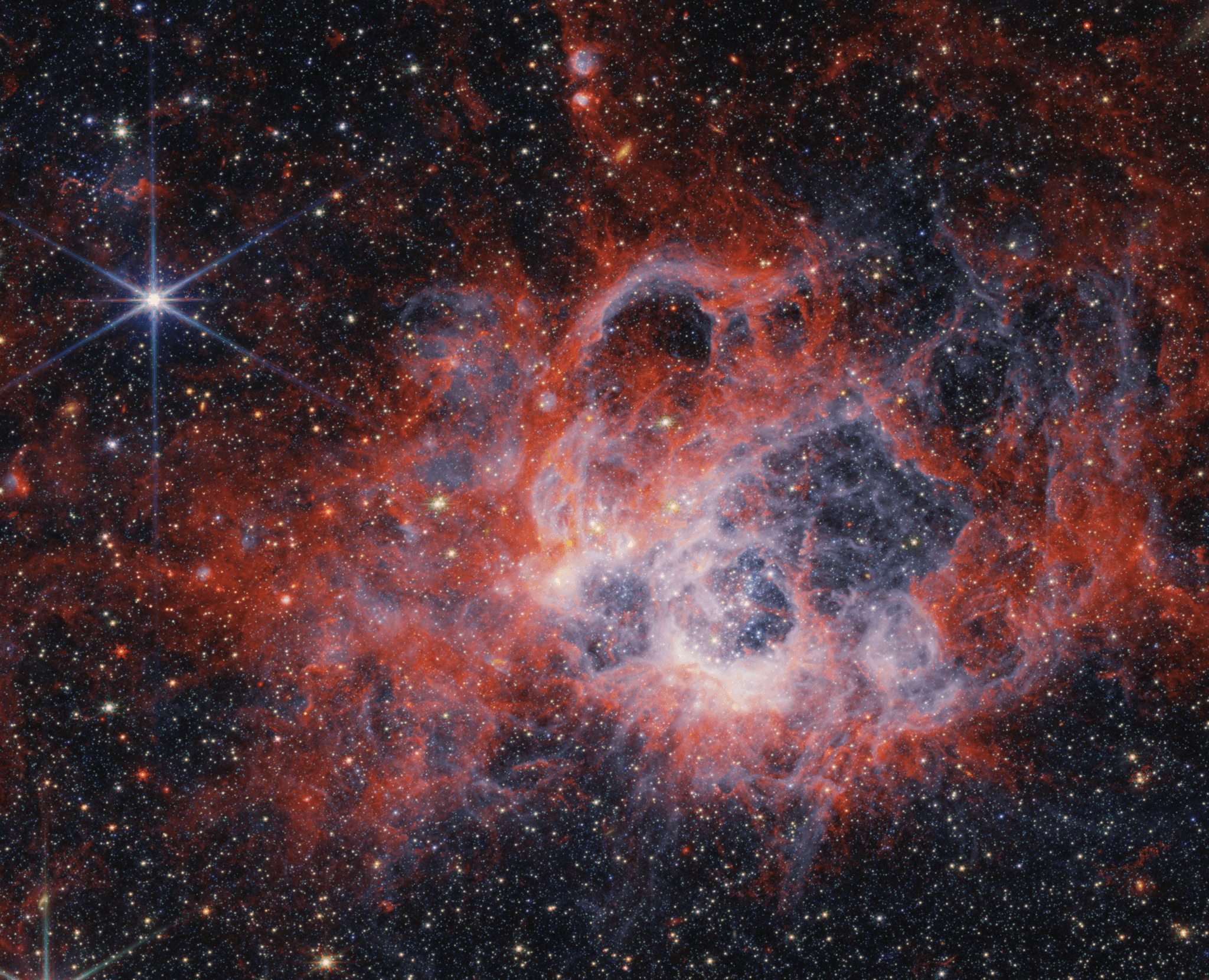 امتداد سديمي محمرّ بمعظمه مع وجود مناطق مبيضّة وتجاويف، تظهر نجومٌ عبر الصورة