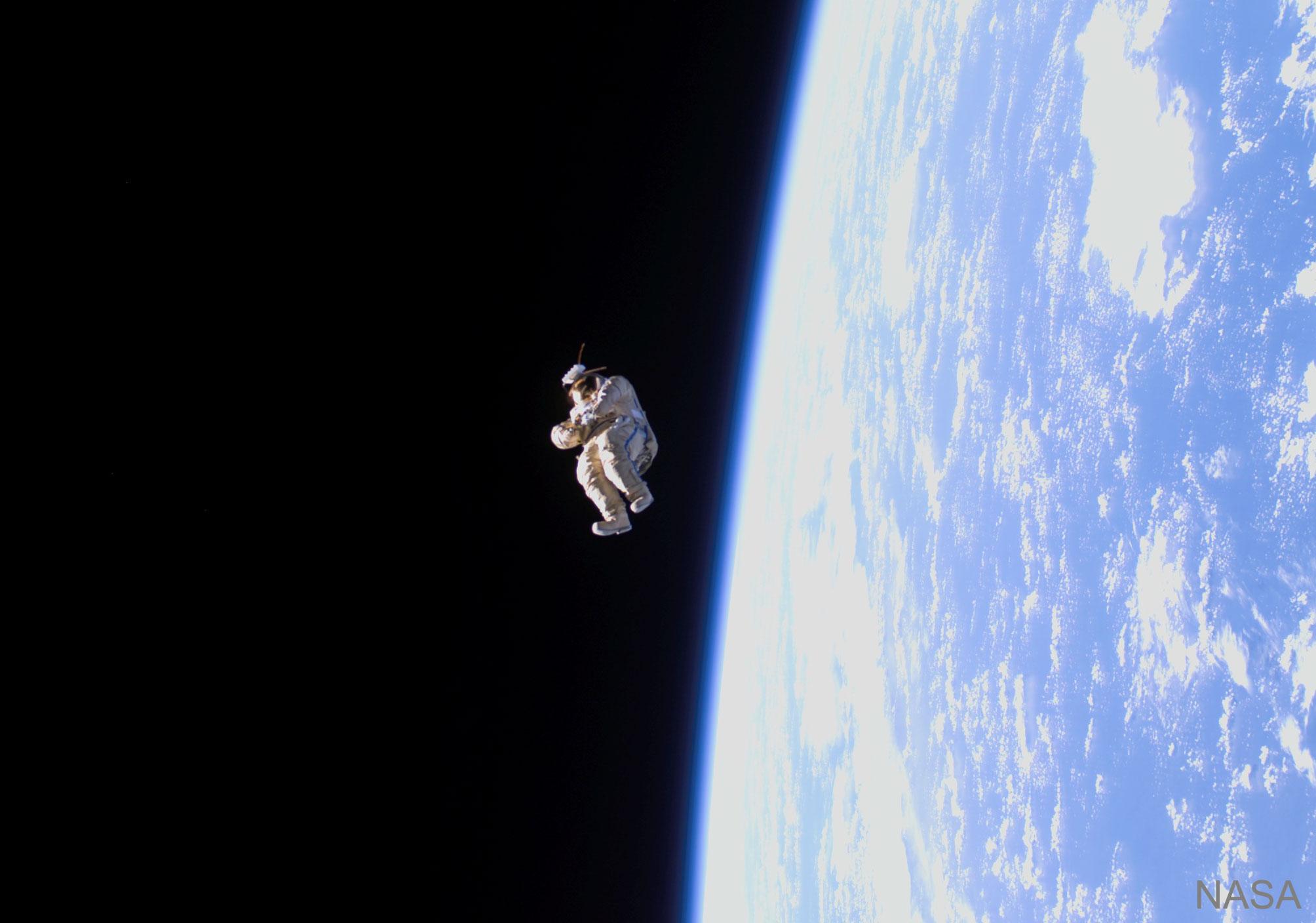 بدلة فضاء تطوف لوحدها بعيداً في منتصف الصورة ومن خلفها الفضاء الحالك ويظهر في نصف الصورة الأيمن كوكب الأرض الأزرق بغيومه البيضاء