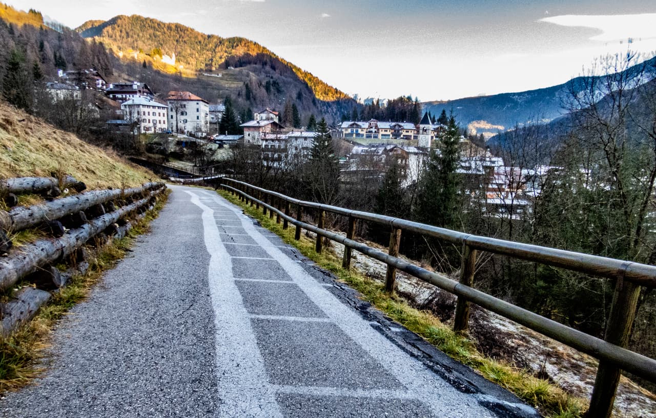 طريق ريفي بسياج على يمينه يظهر مسقطه مرسوماً على الإسفلت كمناطق صقيع، فيما تظهر بعض الأبنية القريبة والأشجار ومن خلفها التلال